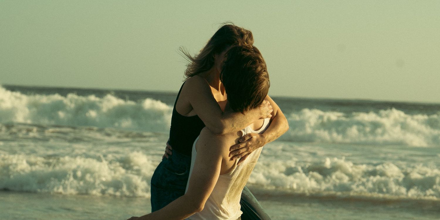 Playful couple dancing on beach with ocean waves in background.