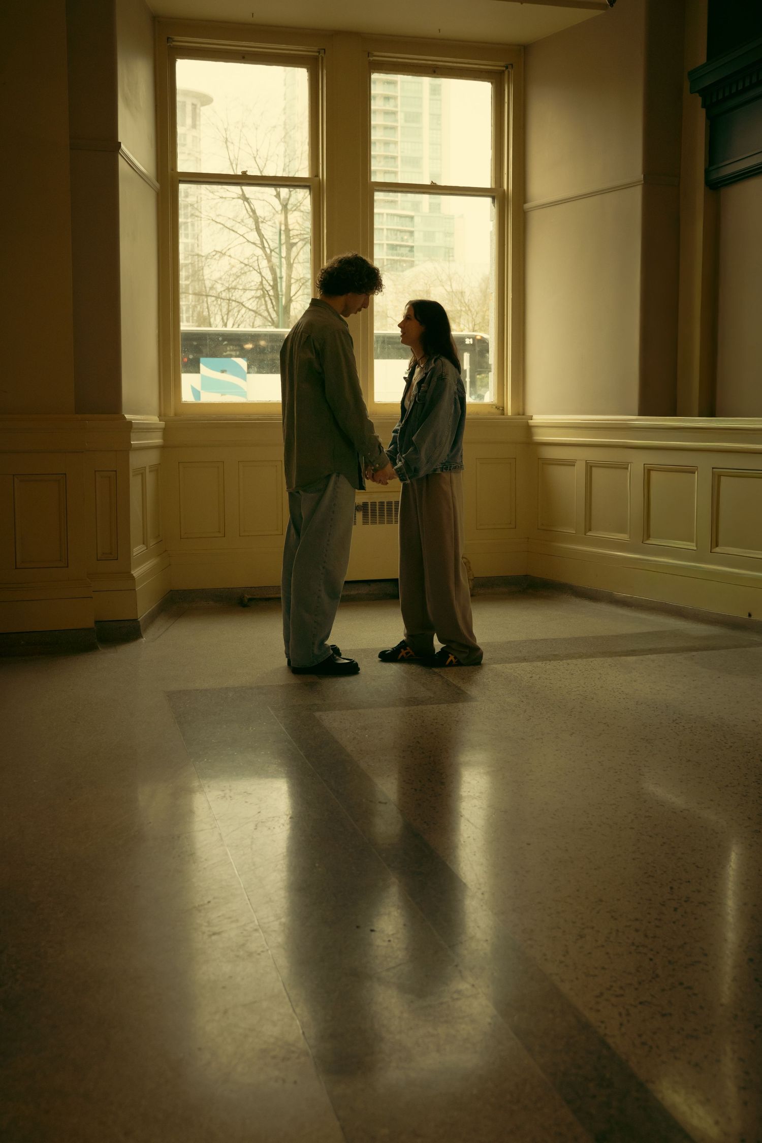 Silhouettes of two people standing in an empty hallway with sunlight streaming through windows.