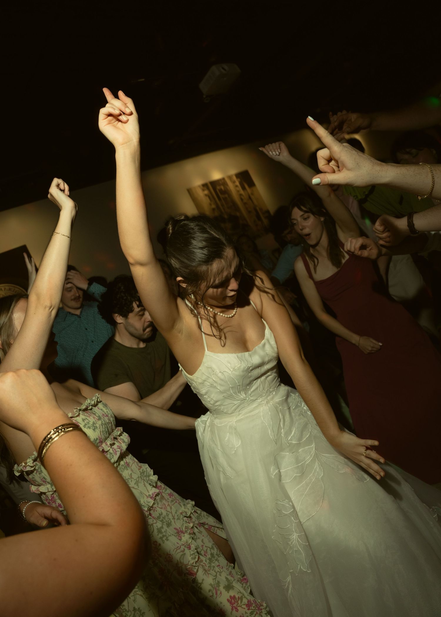 Bride in white wedding gown dancing joyfully with guests at lively wedding reception party.