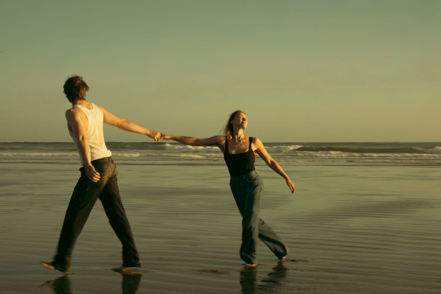 Two people holding hands while dancing on beach at sunset.
