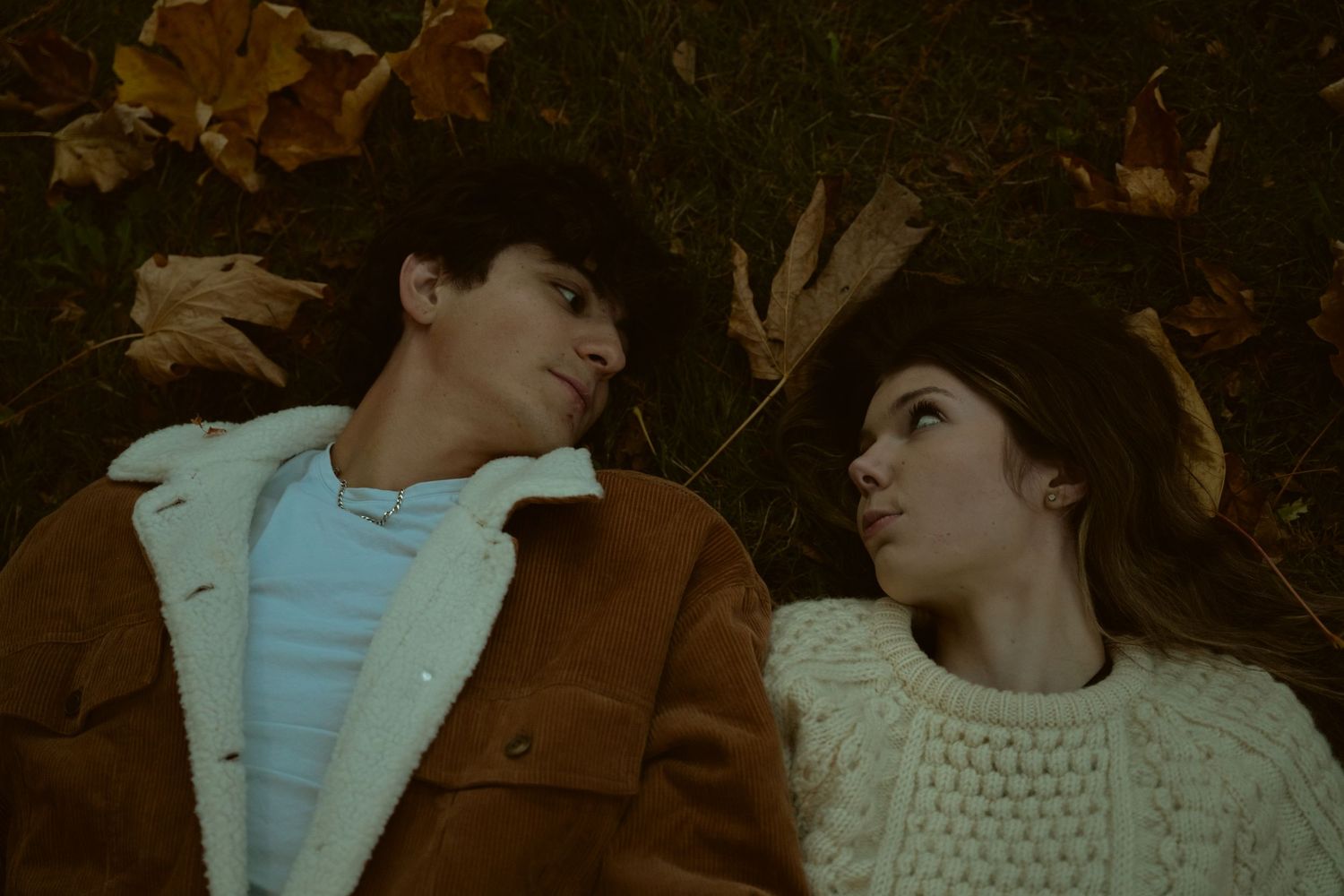 Couple sharing tender moment while lying on autumn ground.