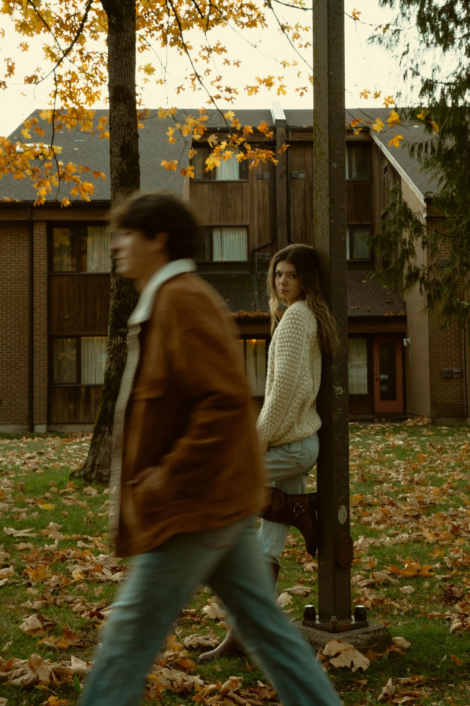 People walking past trees with golden autumn leaves in a residential area.