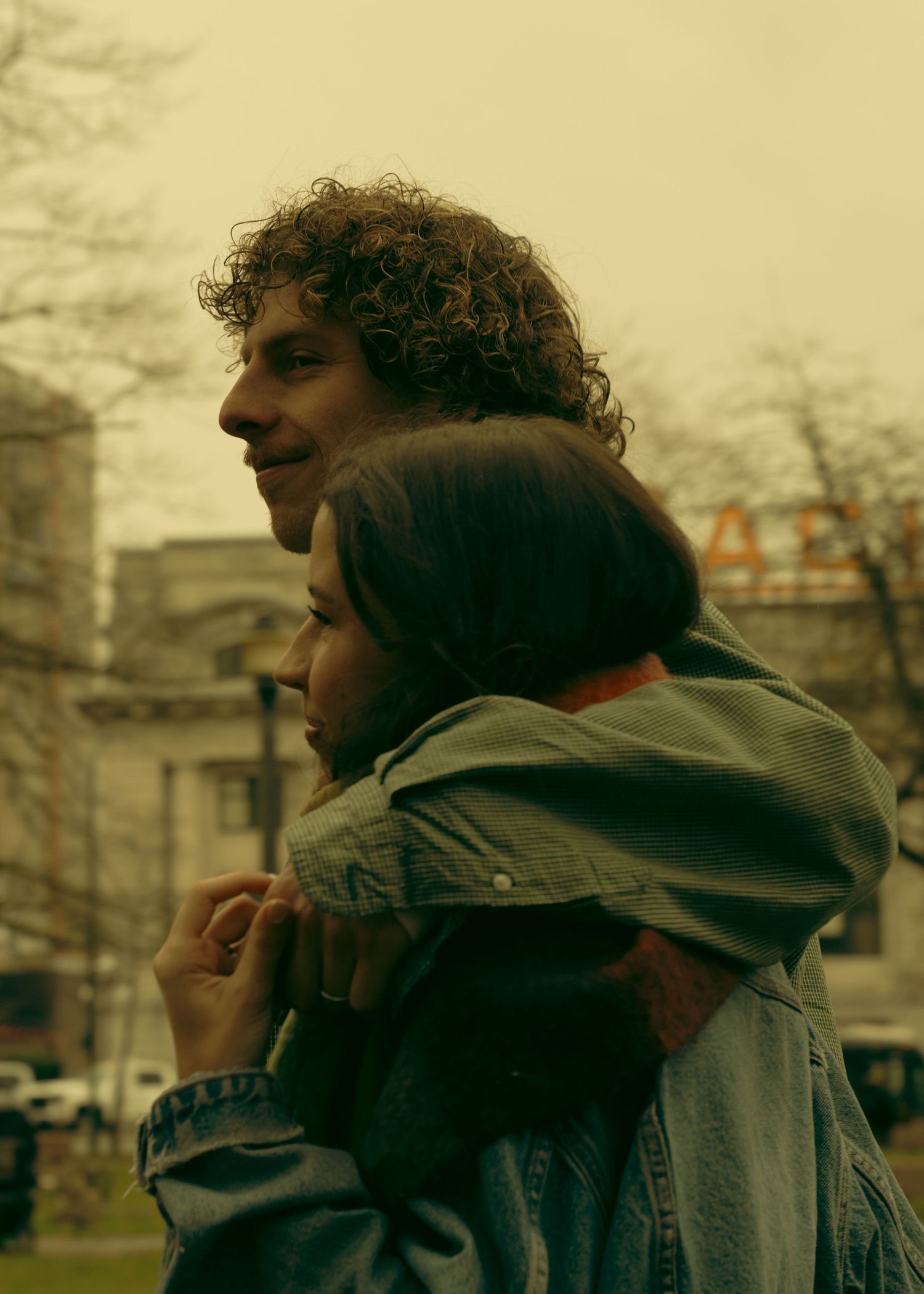 Two people share a close moment outdoors in casual clothing with an autumn backdrop.