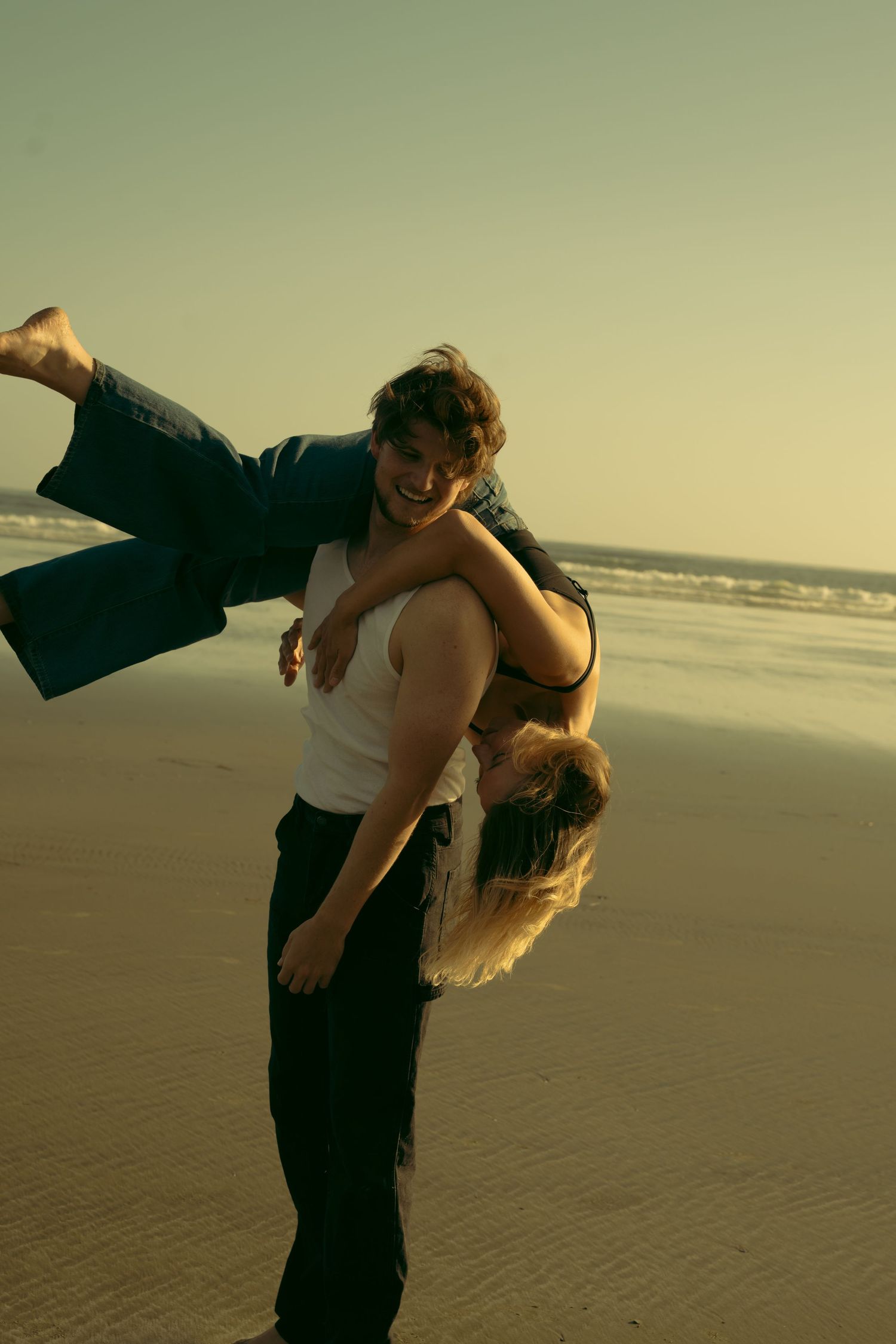 Two people perform a romantic dance move on a sandy beach at dusk.