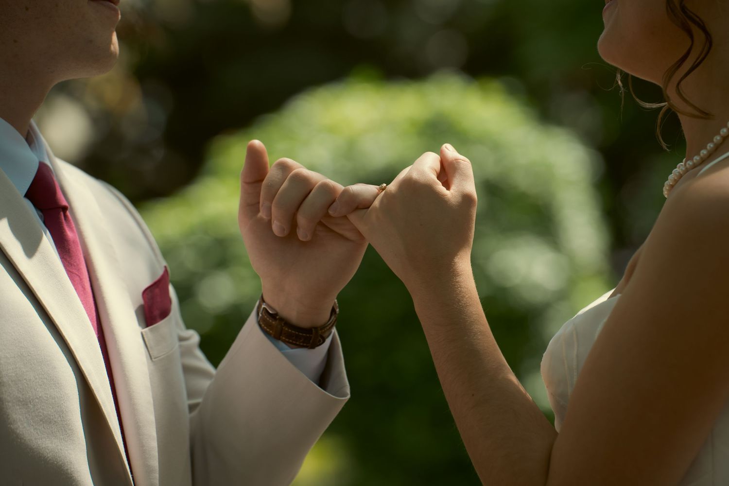 Close-up of bride and groom holding hands during wedding ceremony, groom wearing white suit with red tie.