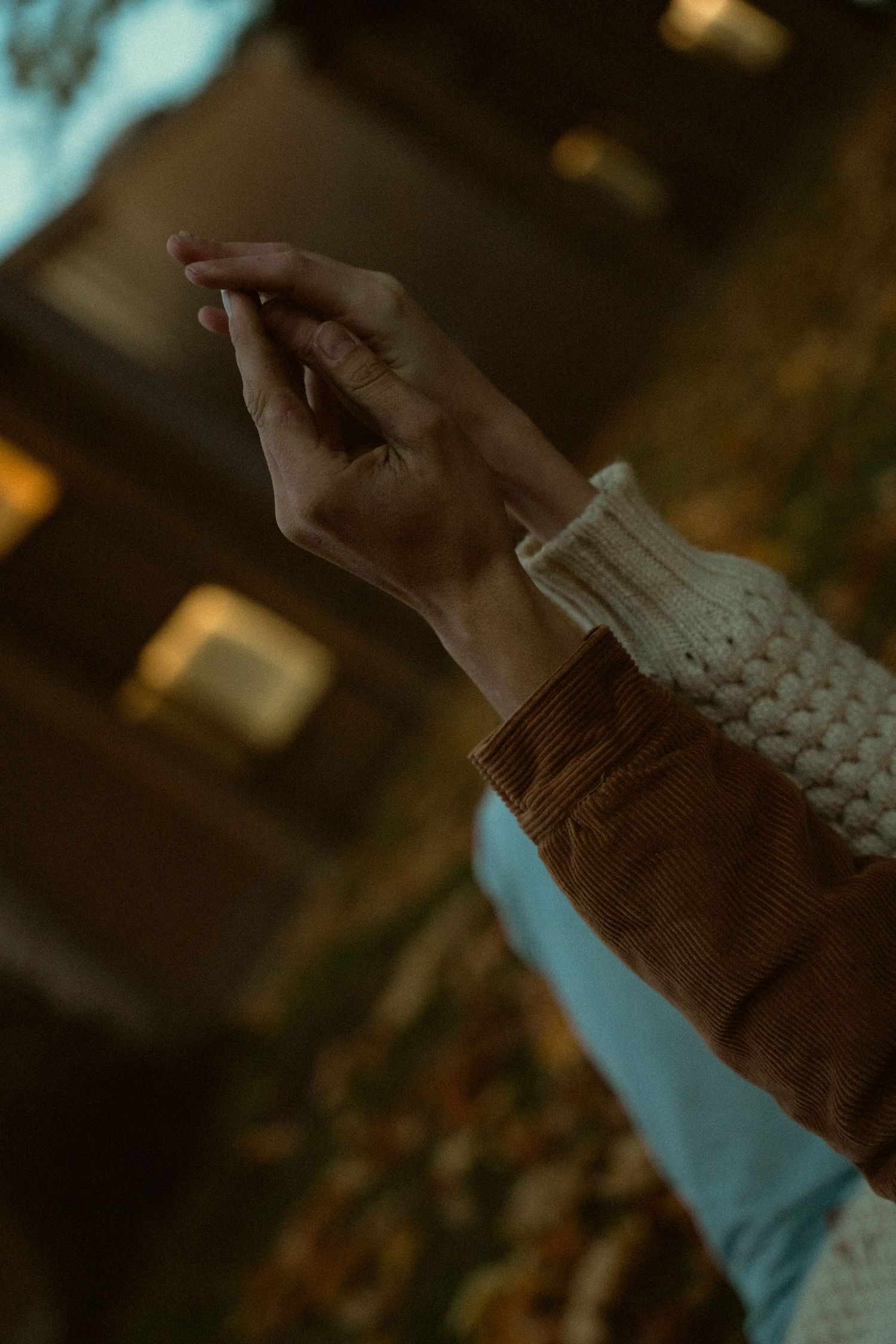 Close-up of hands wearing a knit sweater against a dark autumn background.