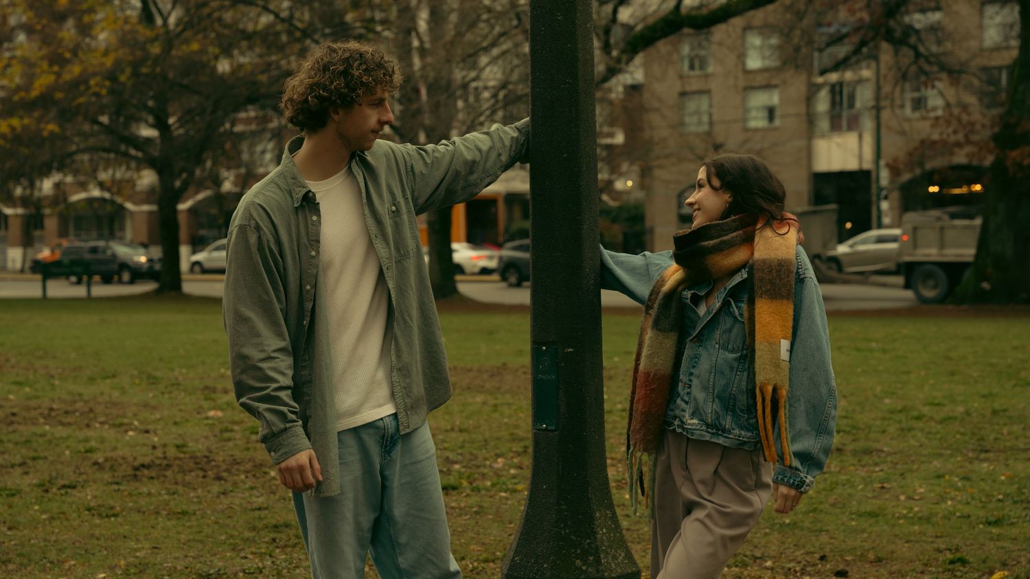 People walking past lamp posts in an urban park during fall season.