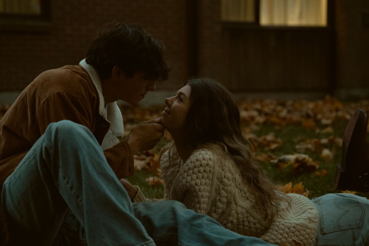 Intimate moment between two people lying on grass near brick building.