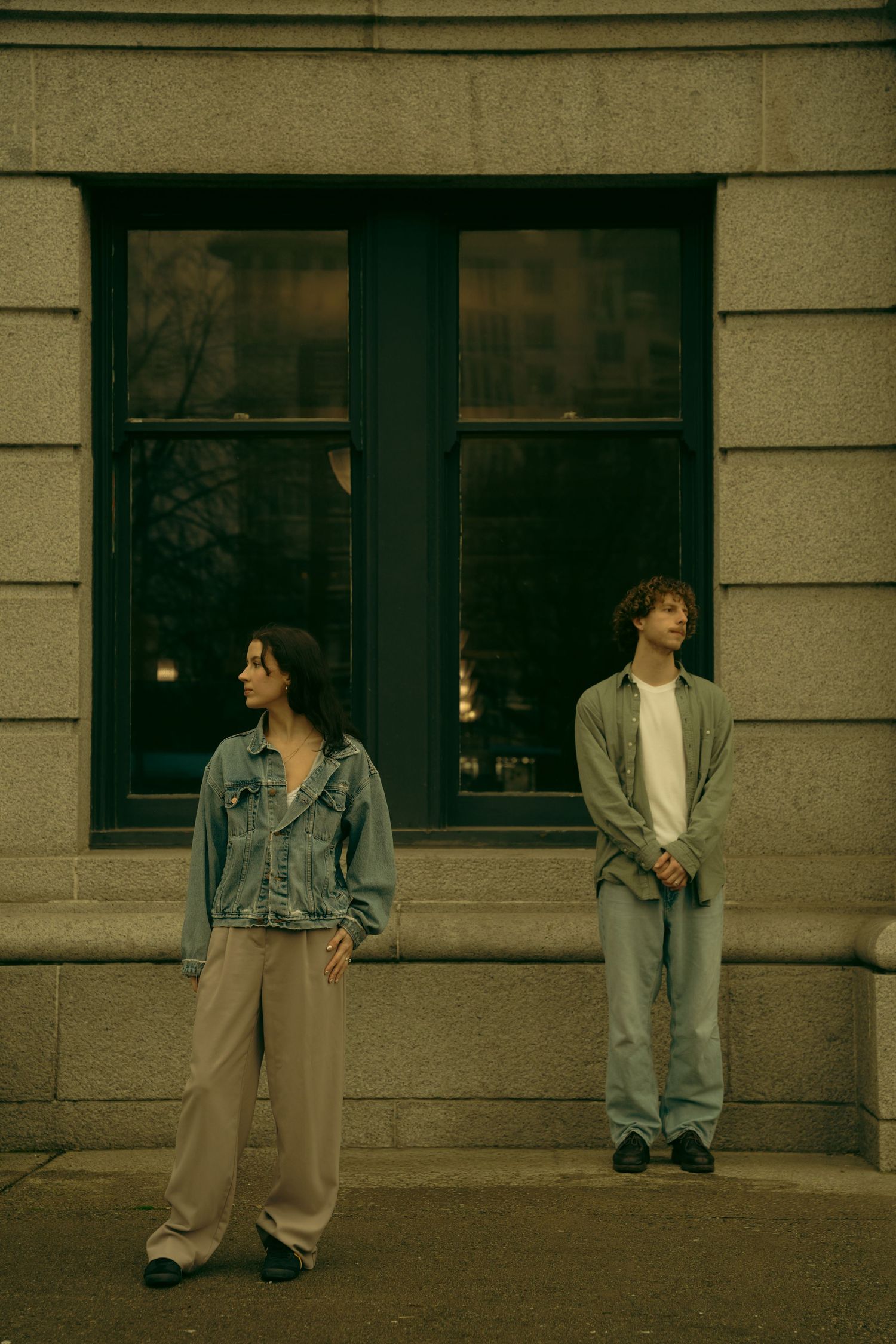 A couple in denim and casual wear poses against a stone building exterior.