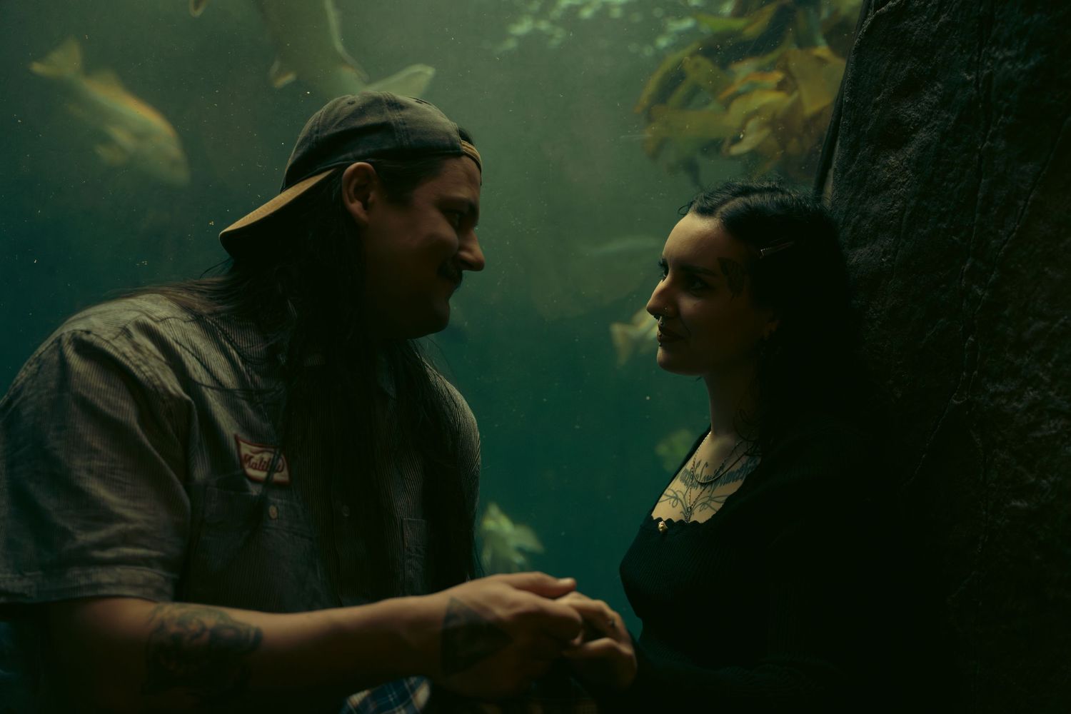 Couple sharing a romantic moment near an aquarium tank with fish and rocks in the background.