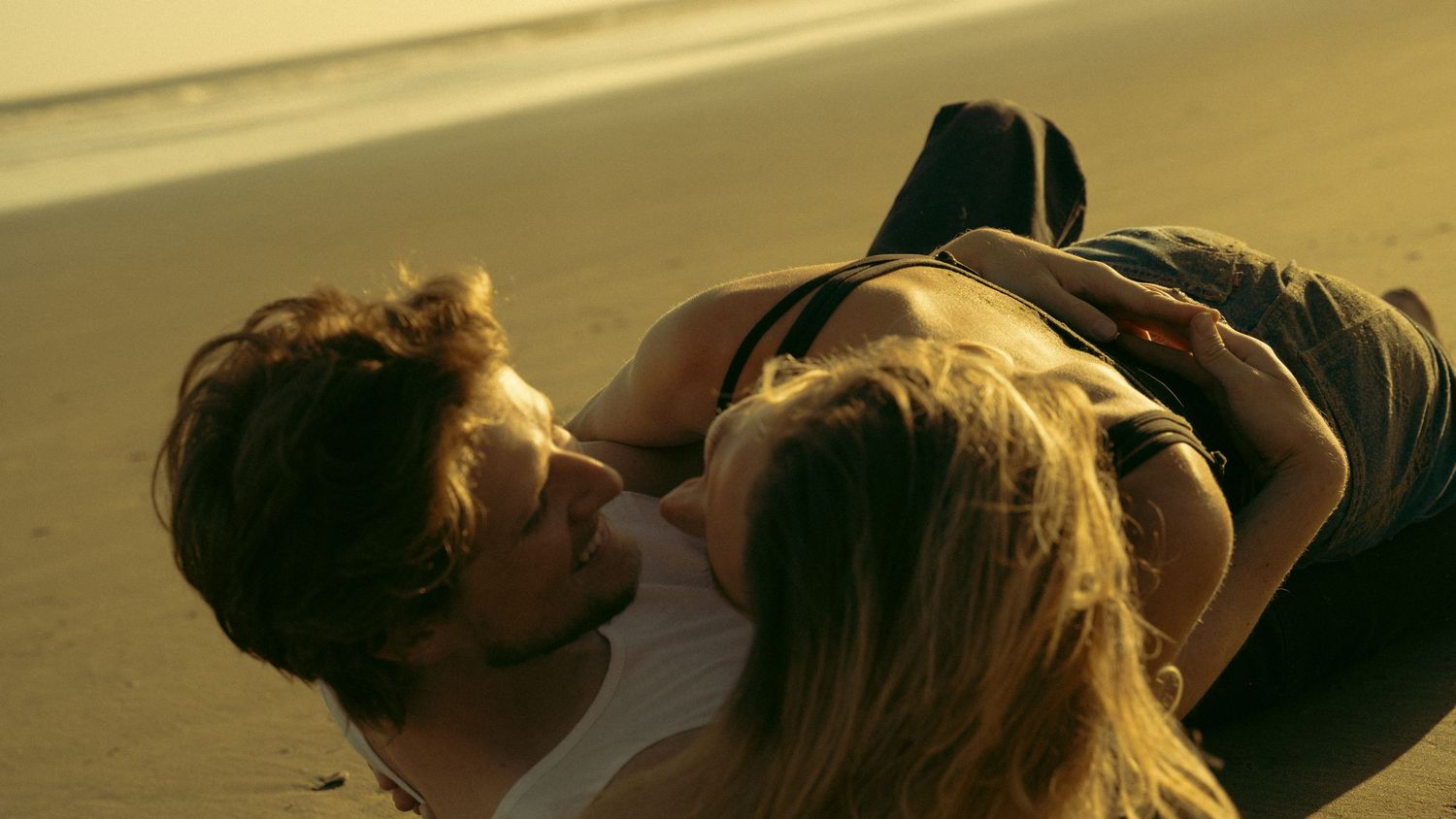 Couple lying together on beach at sunset in intimate pose.