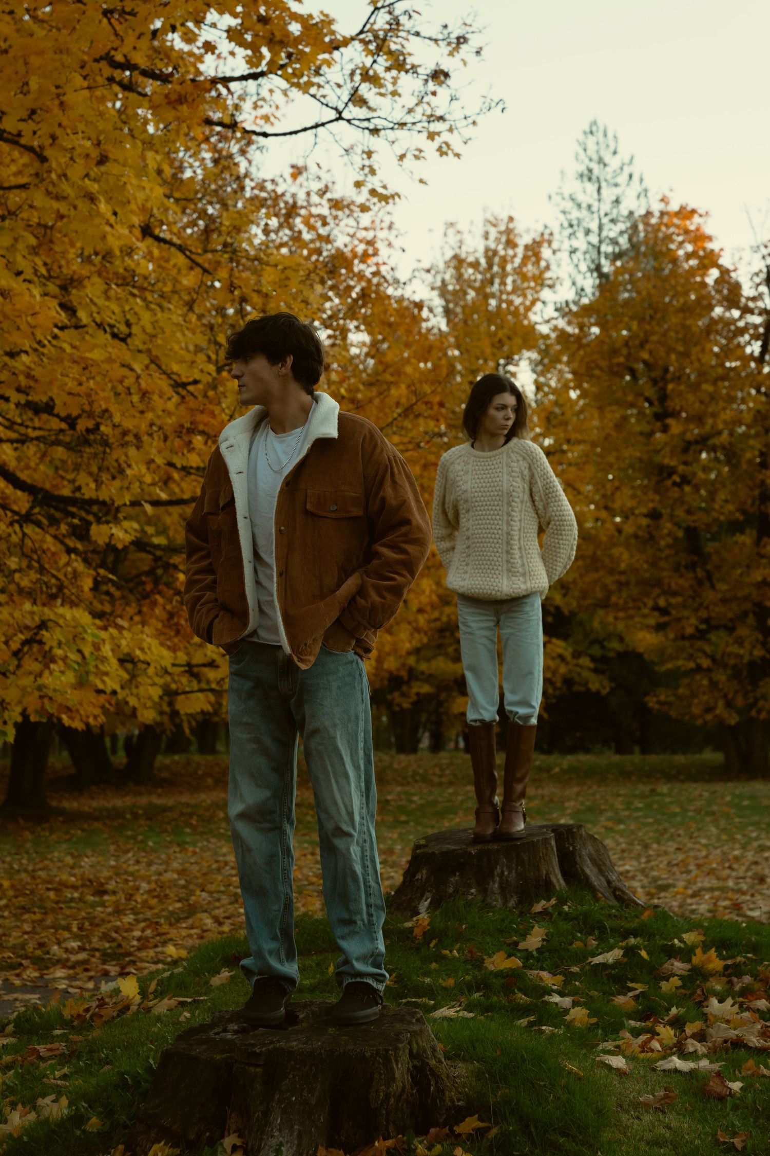 People walking through a park filled with fallen autumn leaves at sunset.