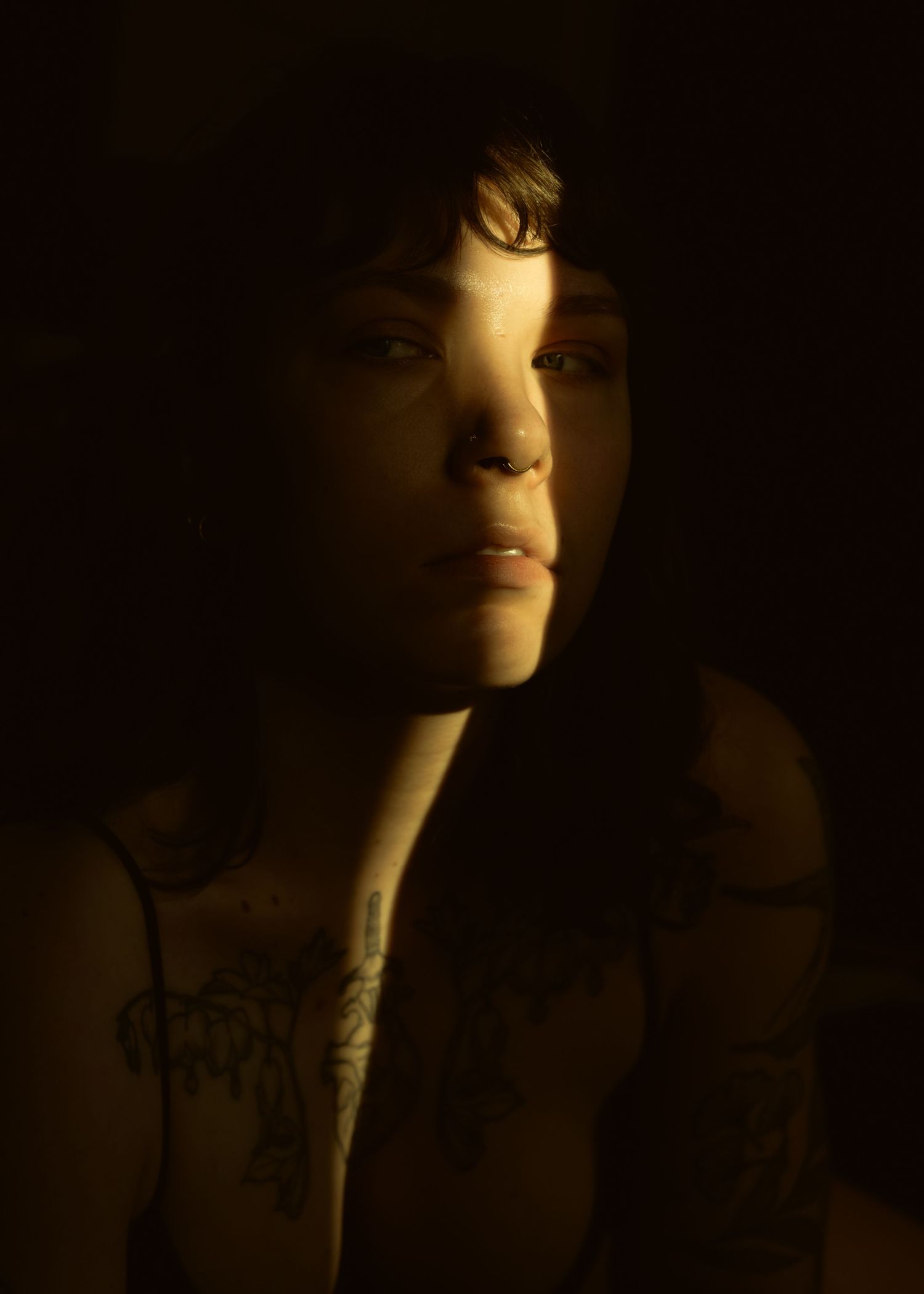 Dramatic low-key portrait in chiaroscuro lighting shows a figure's face emerging from deep shadows.