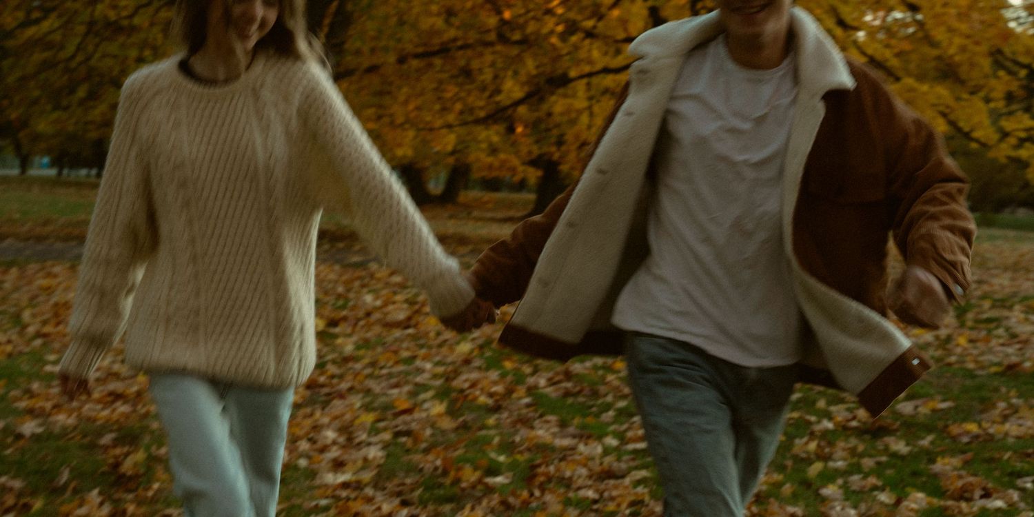 People walking through autumn leaves on ground in casual attire.