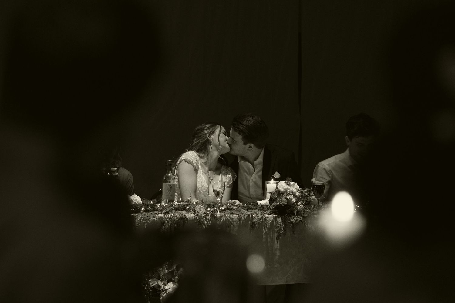 Black and white reception photo of couple at head table with bokeh lighting effects.