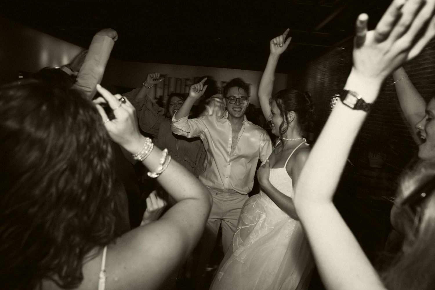 Black and white photo of wedding guests dancing joyfully at a lively reception party.