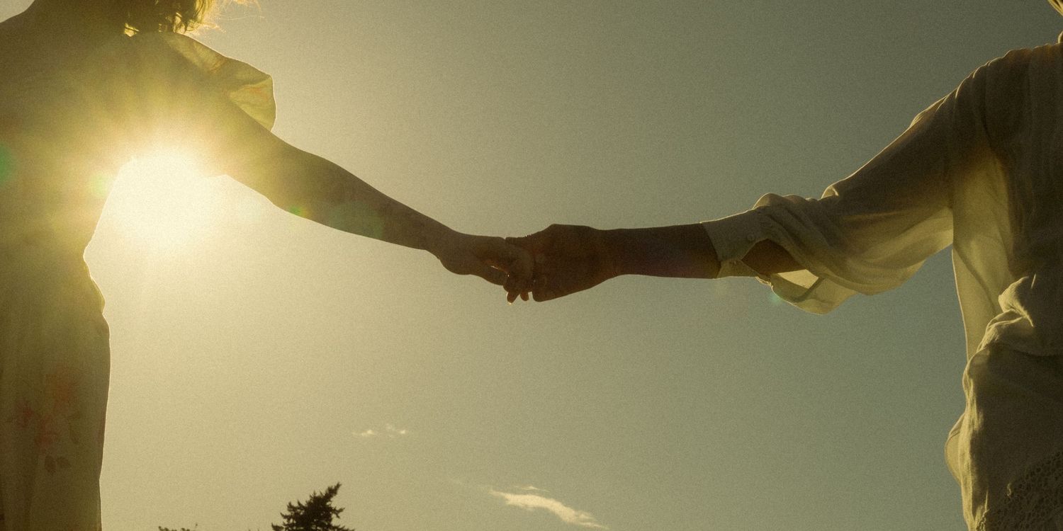 Two people holding hands against a golden sunset sky, symbolizing connection and togetherness.