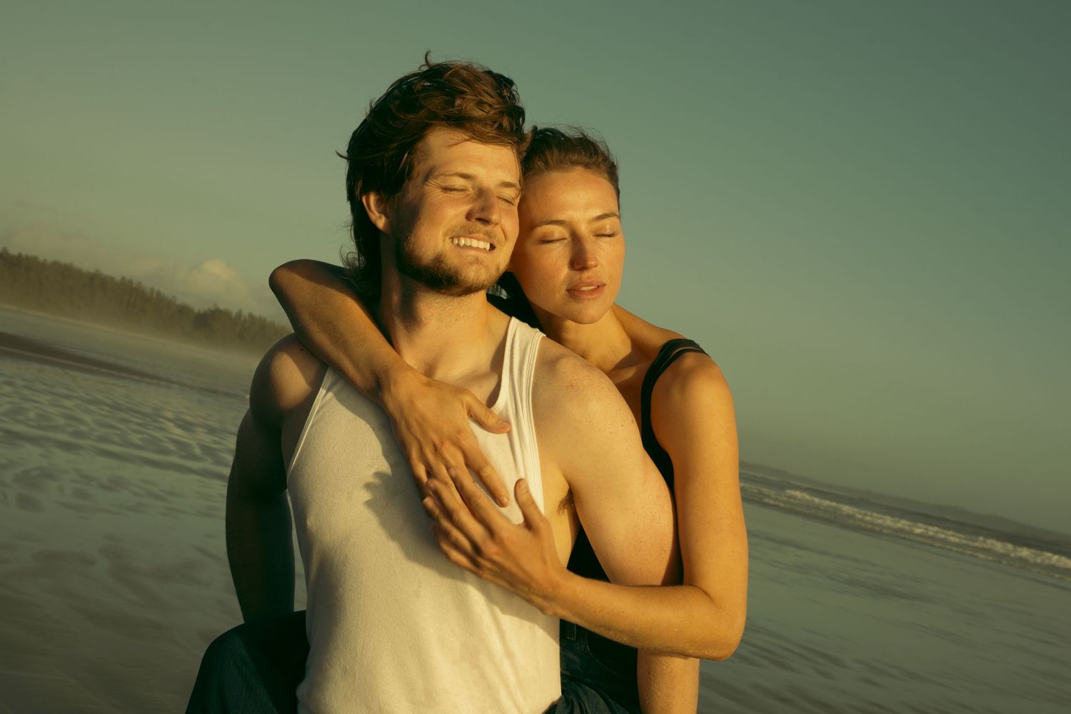 Couple embracing on beach at sunset with golden light.