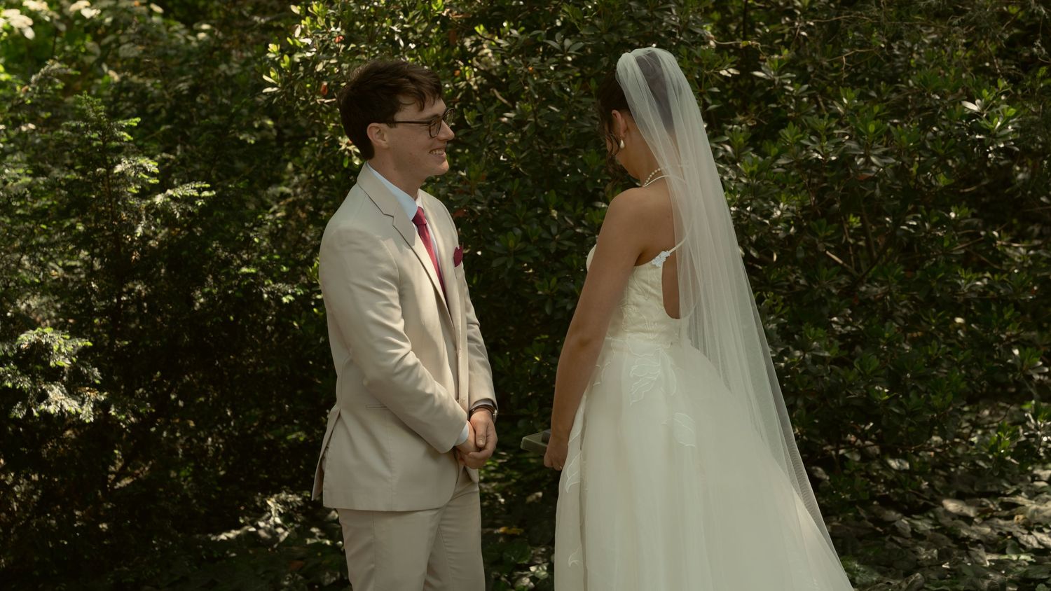 Bride and groom hold hands and share a moment in lush green outdoor wedding setting.