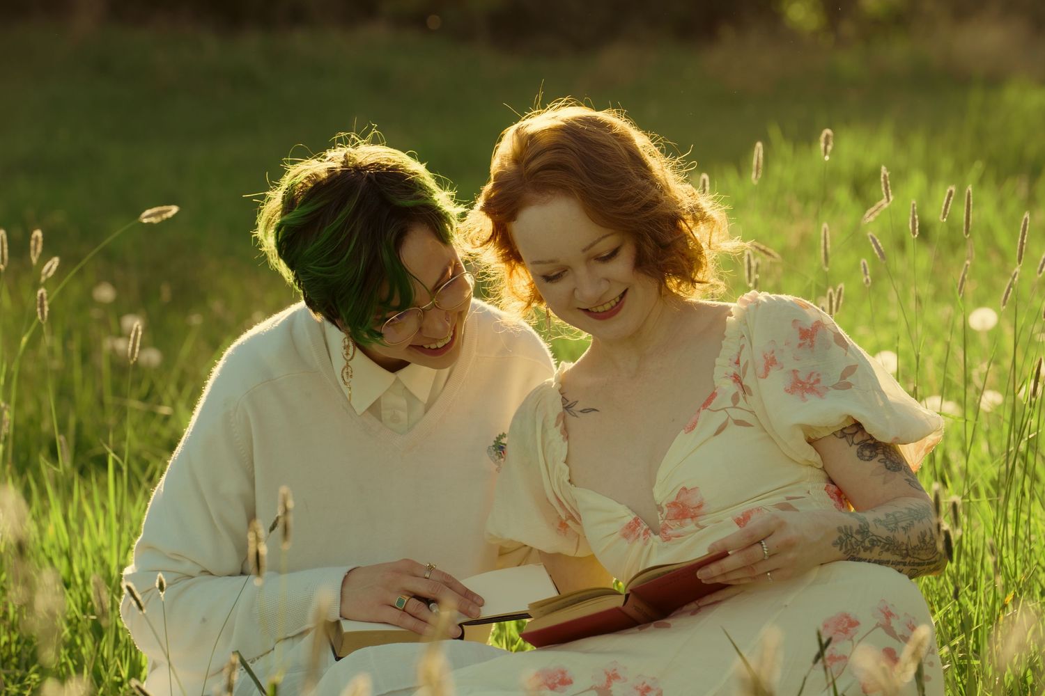 Two people in white outfits read a book together in a sunlit green meadow.