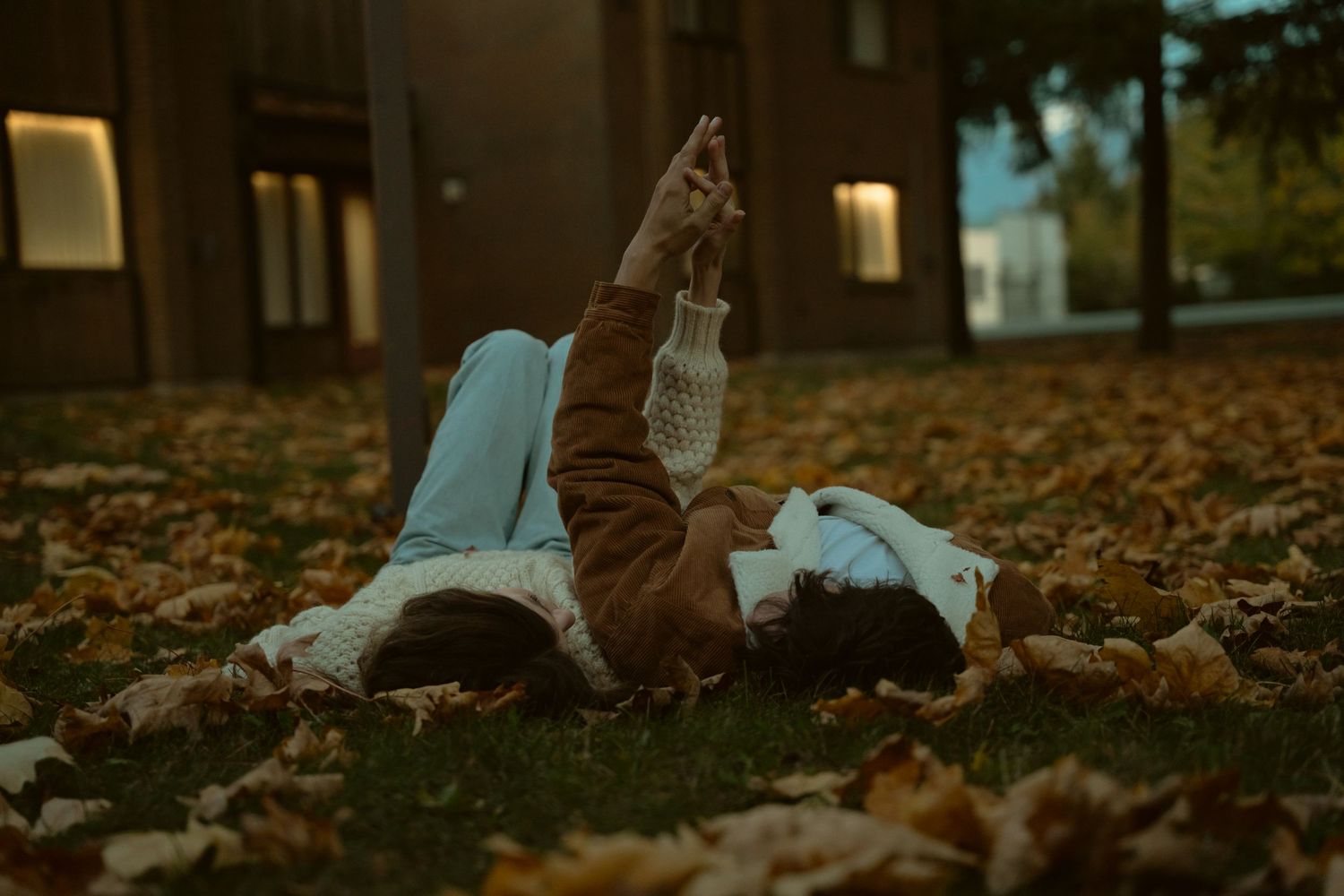 Two people lying on autumn leaves gazing up at the sky at dusk.