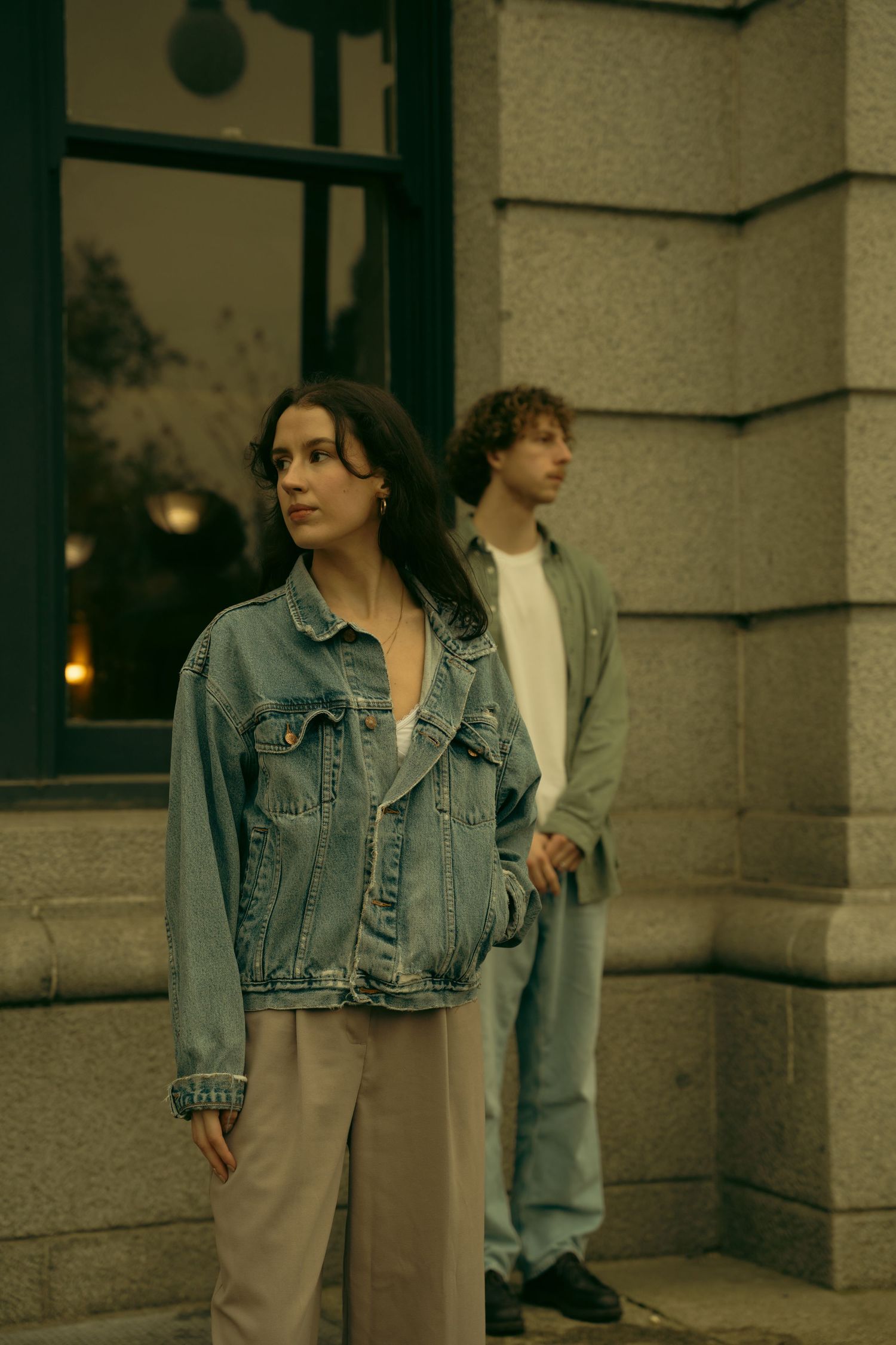 A couple in retro clothing stands against an urban building backdrop.