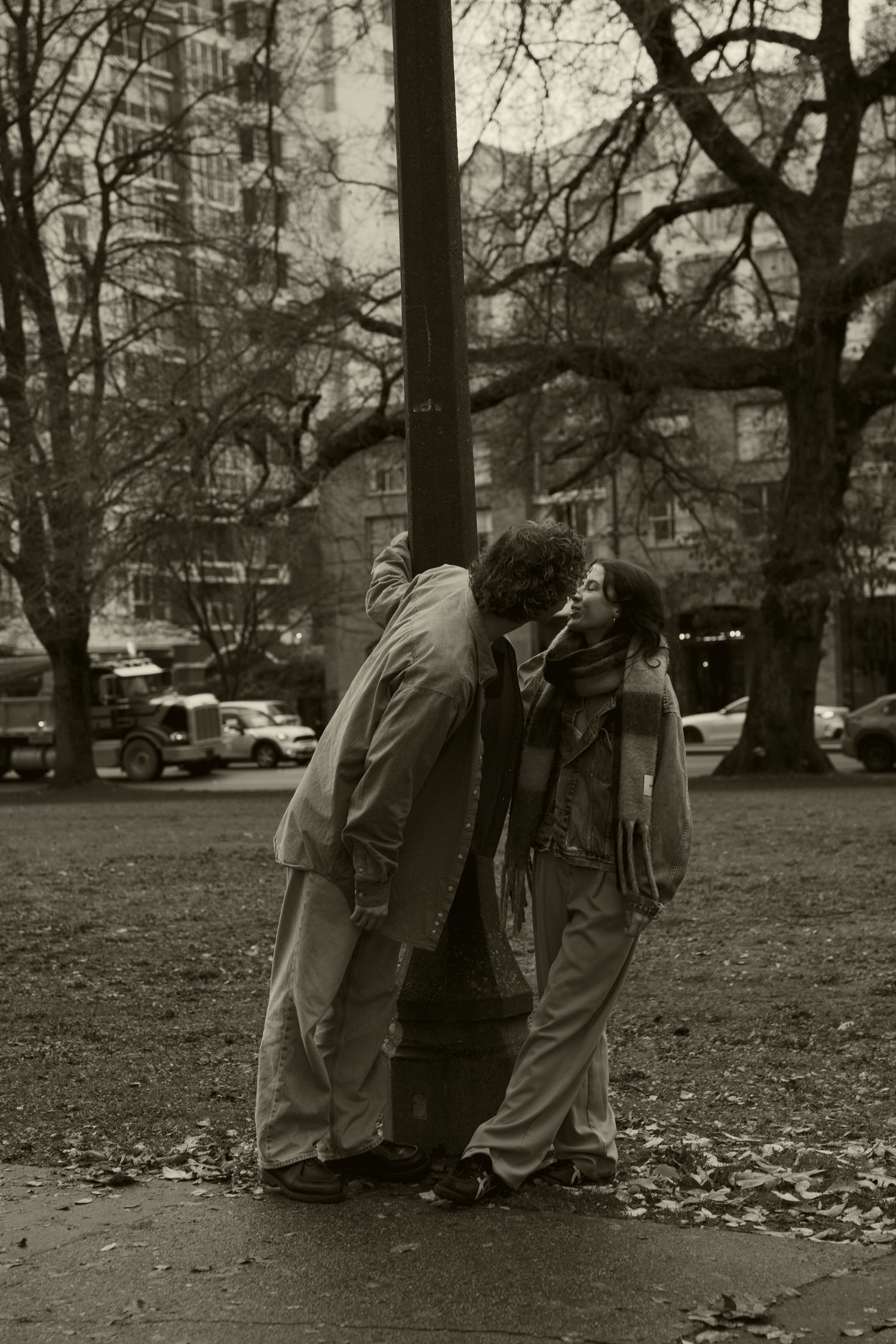 People gathered in a park on a cloudy autumn day with fallen leaves on the ground.