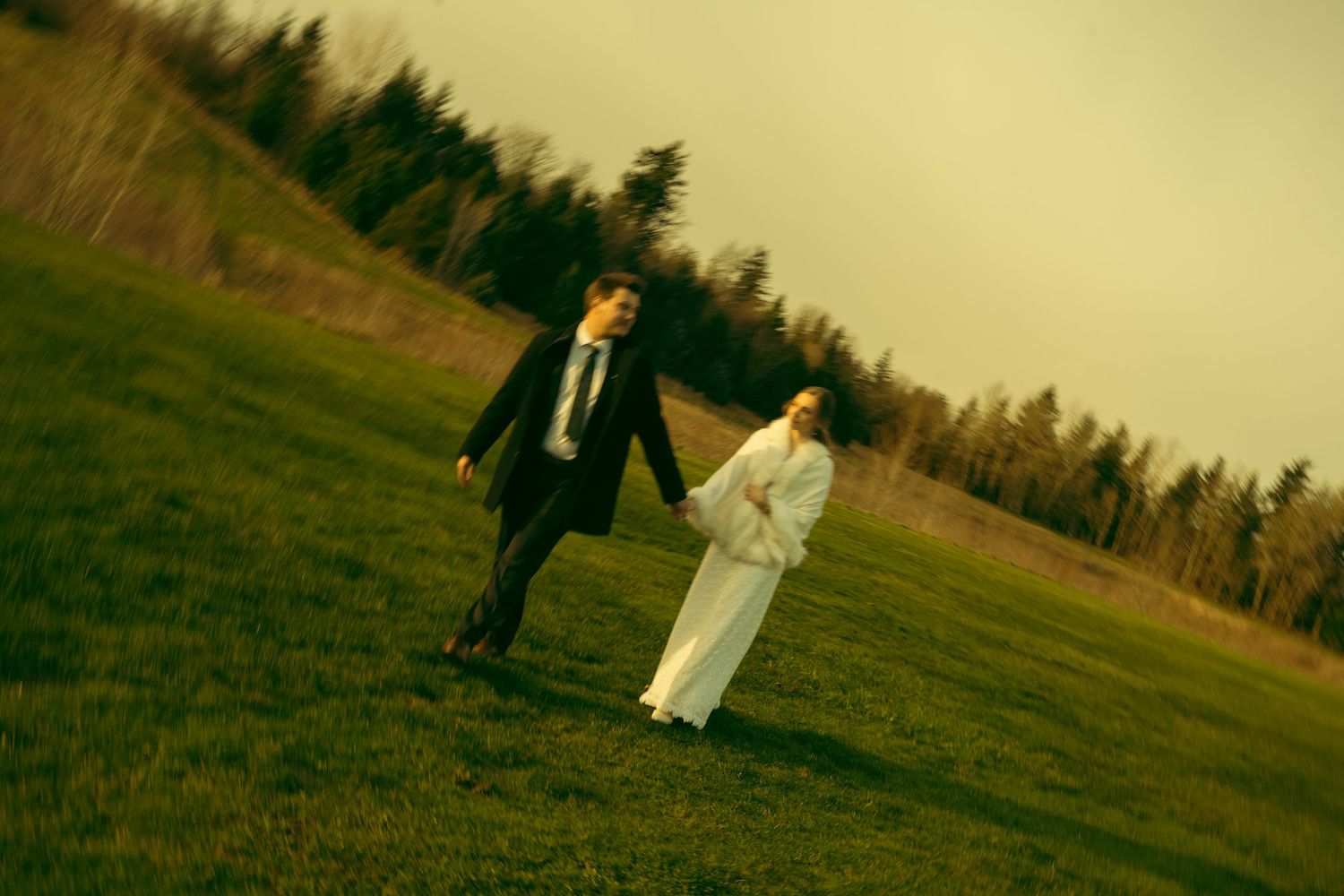 Newlyweds walking together across a scenic grassy field at dusk.