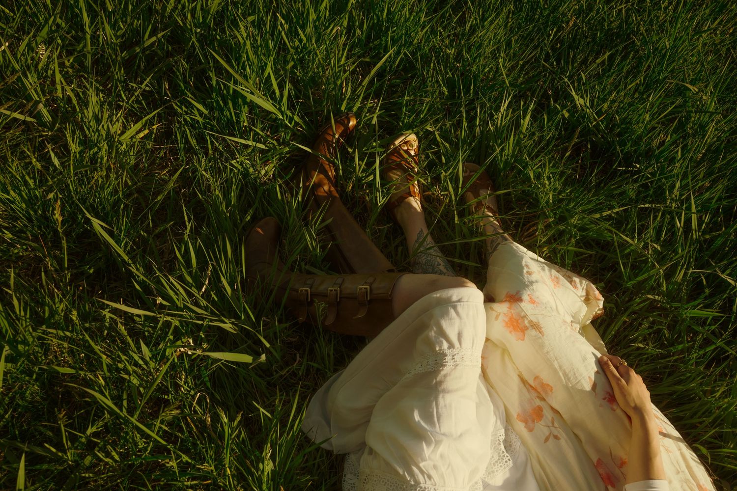 Close-up of two people lying in lush green grass wearing floral dress and colorful shoes.