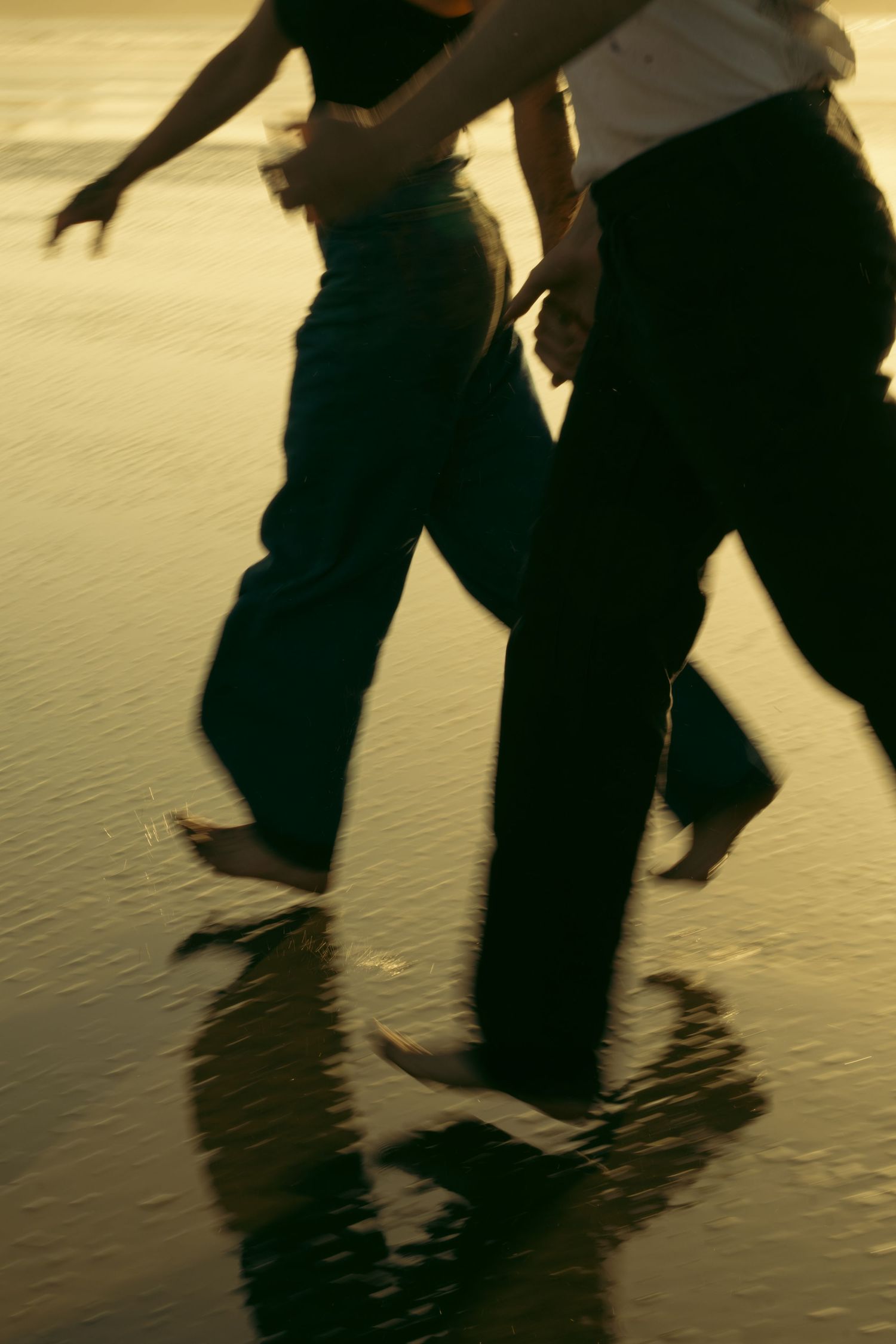 Silhouetted figures dancing on wet sand at sunset.