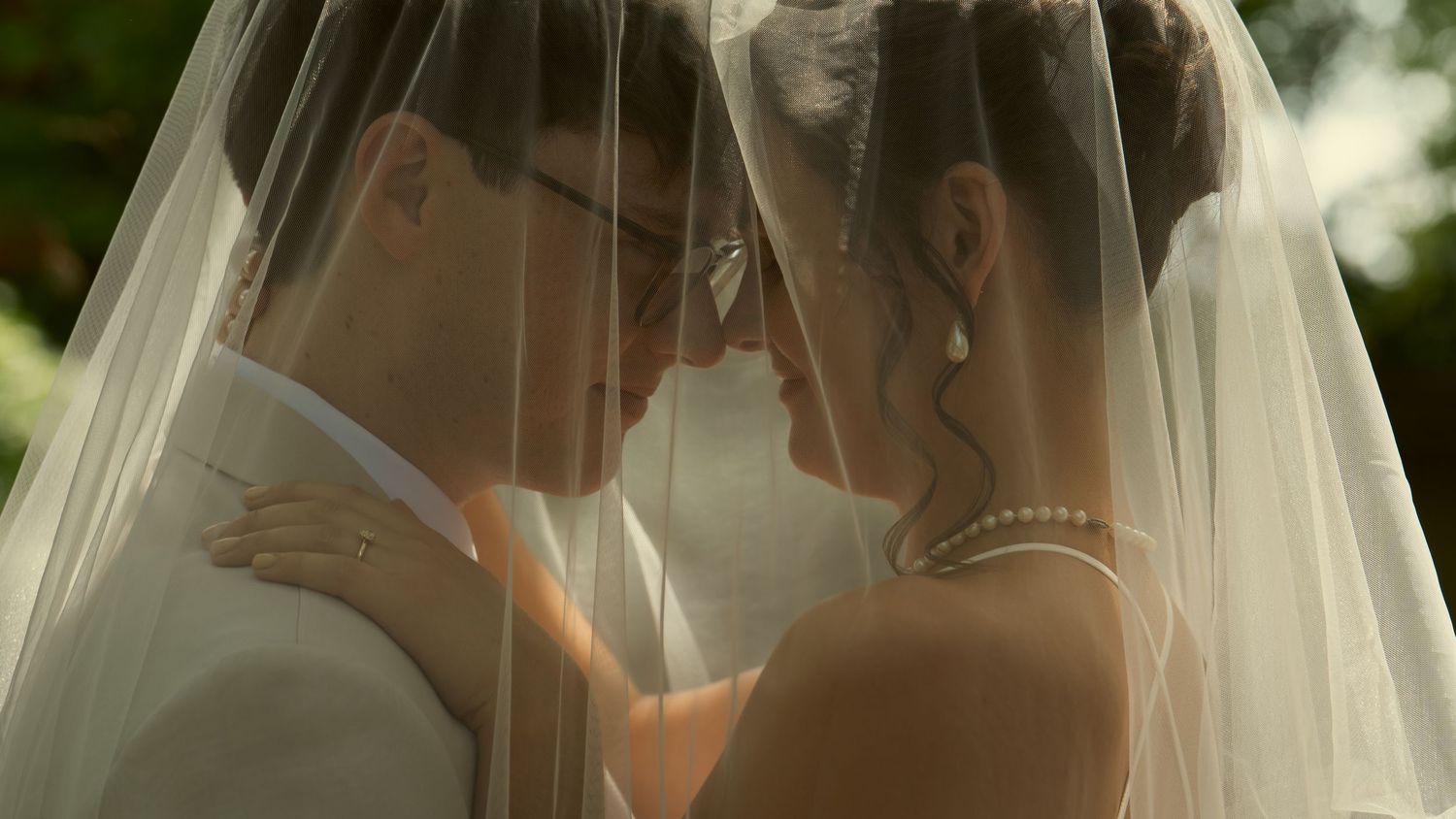Bride and groom sharing an intimate moment under a sheer wedding veil outdoors on their wedding day.