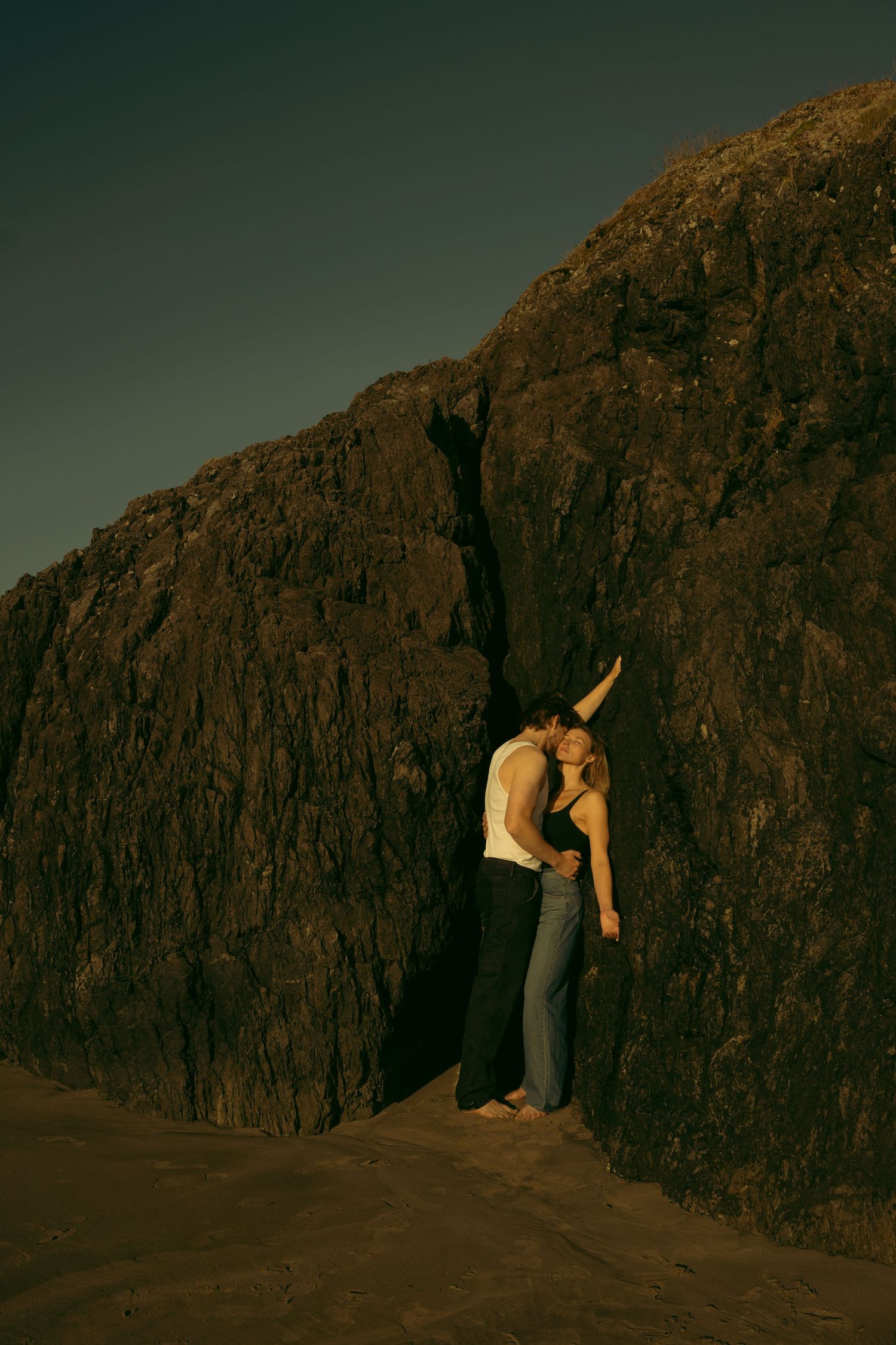 A couple sharing a romantic moment against a towering cliff face at sunset.