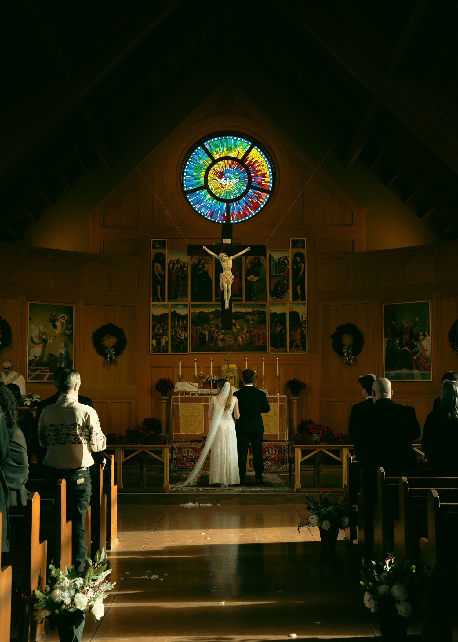 A wedding ceremony takes place in a church sanctuary with stained glass windows and religious artwork on display.