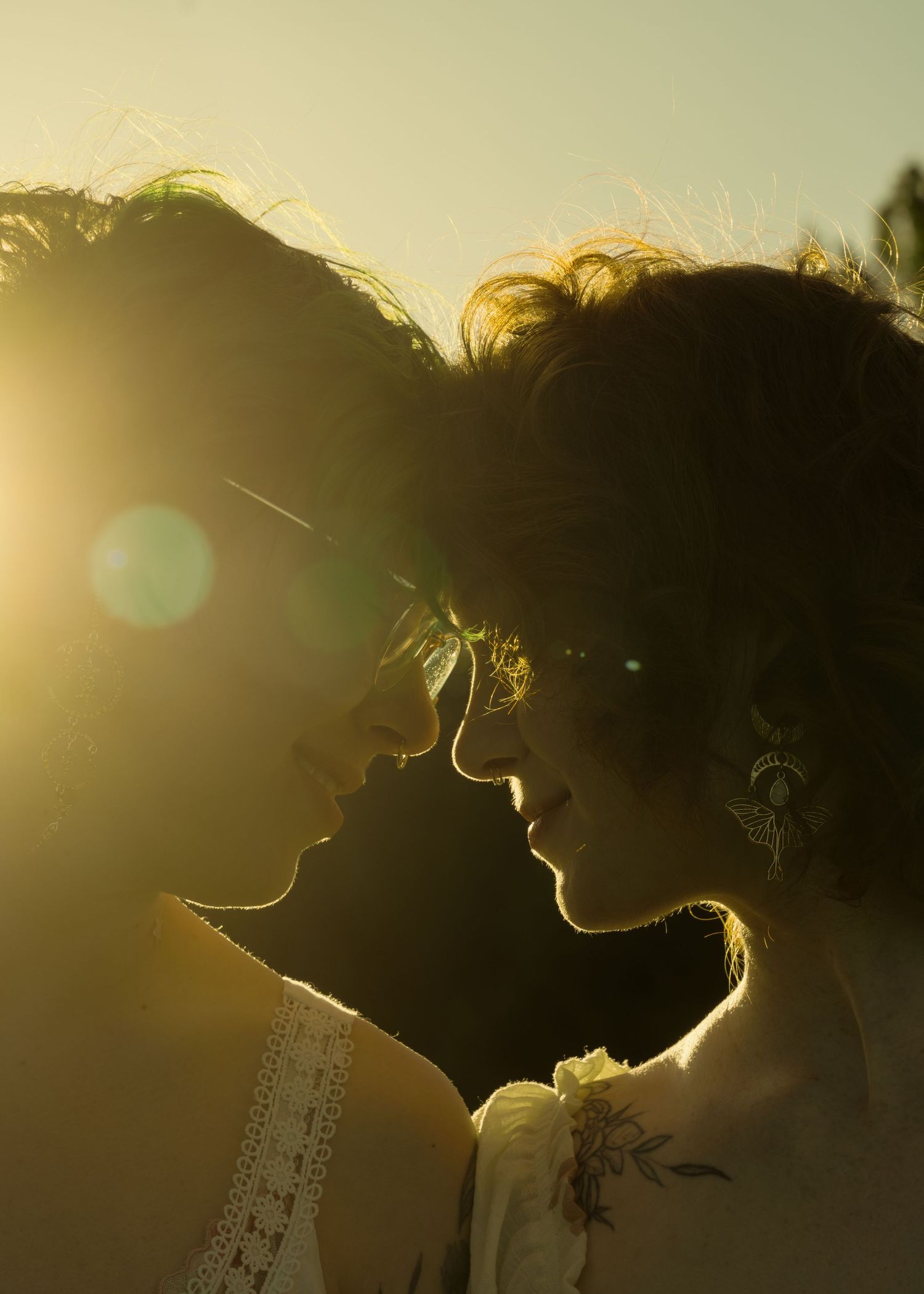 Romantic couple silhouetted against golden sunset light, facing each other in an intimate moment.