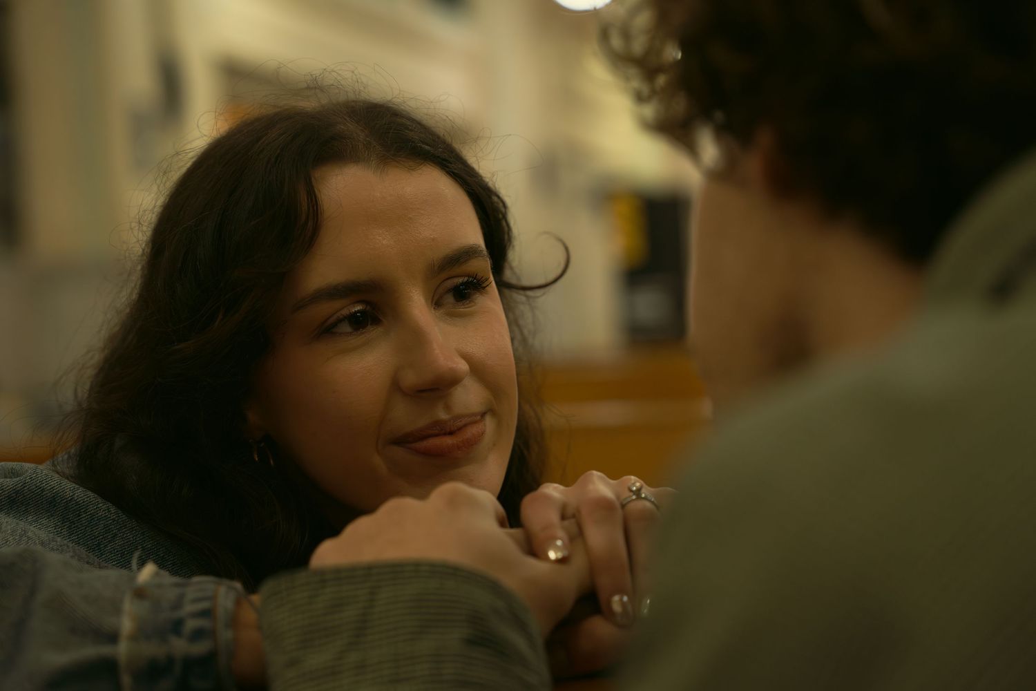 Two people share an intimate conversation in a warmly lit indoor setting.
