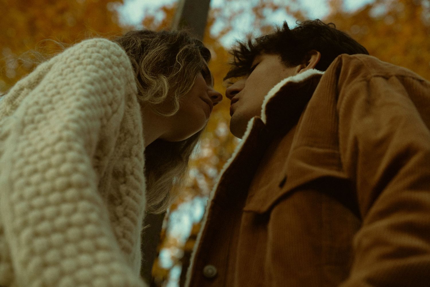 Couple in autumn setting with person wearing cream knit sweater and brown jacket.