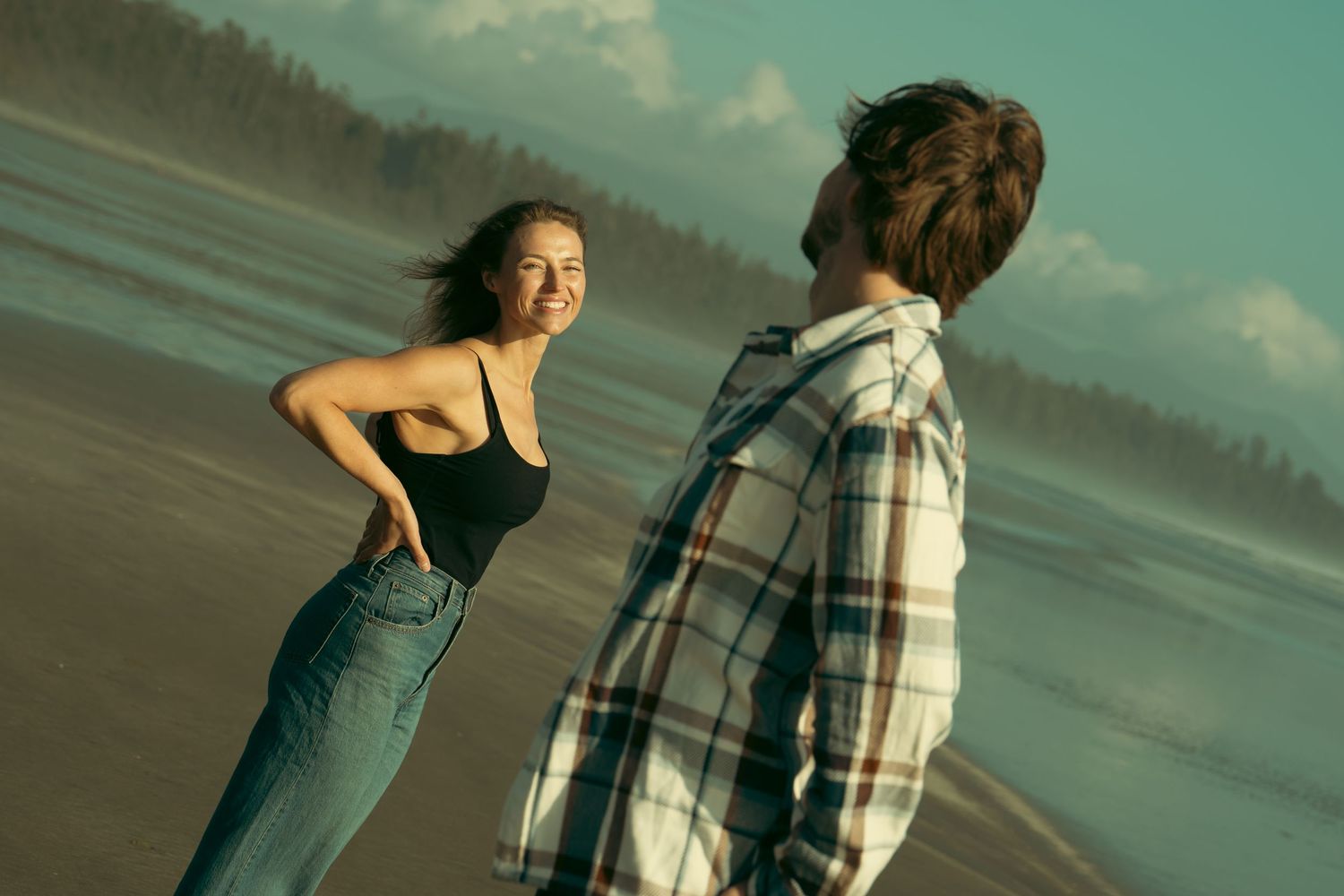 A playful moment between two people on a beach with moody teal tones.