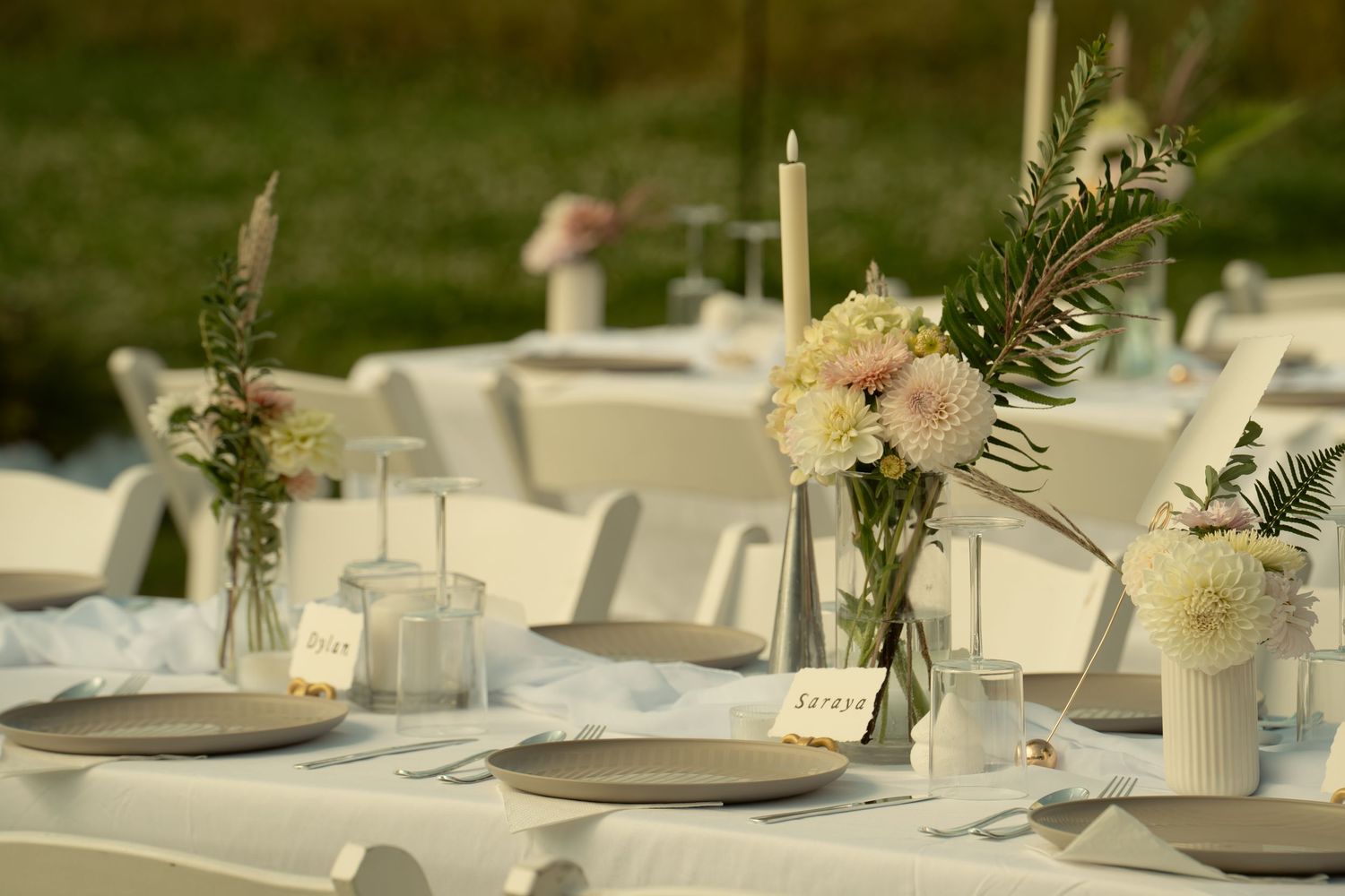Elegant wedding reception table settings with white floral centerpieces, candles and place settings on neutral linens.