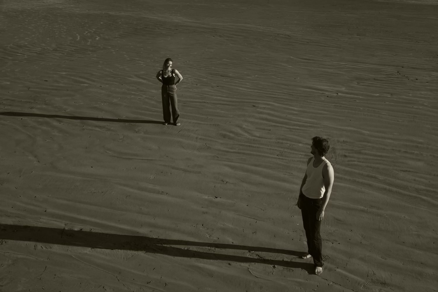 Two silhouettes standing apart on a sandy beach in dramatic lighting.