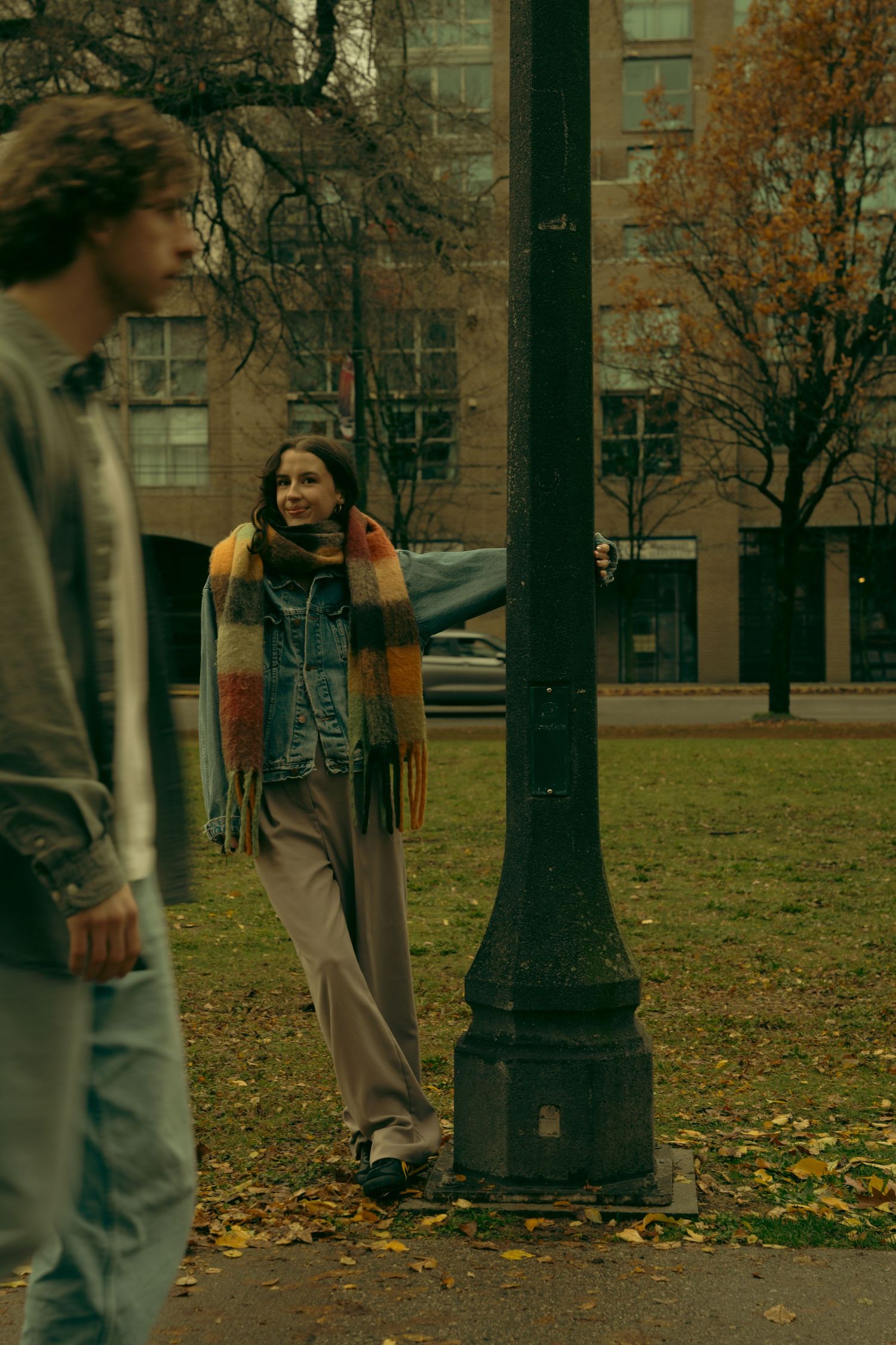 A group walks through a park with vintage lamp posts and fallen autumn leaves.