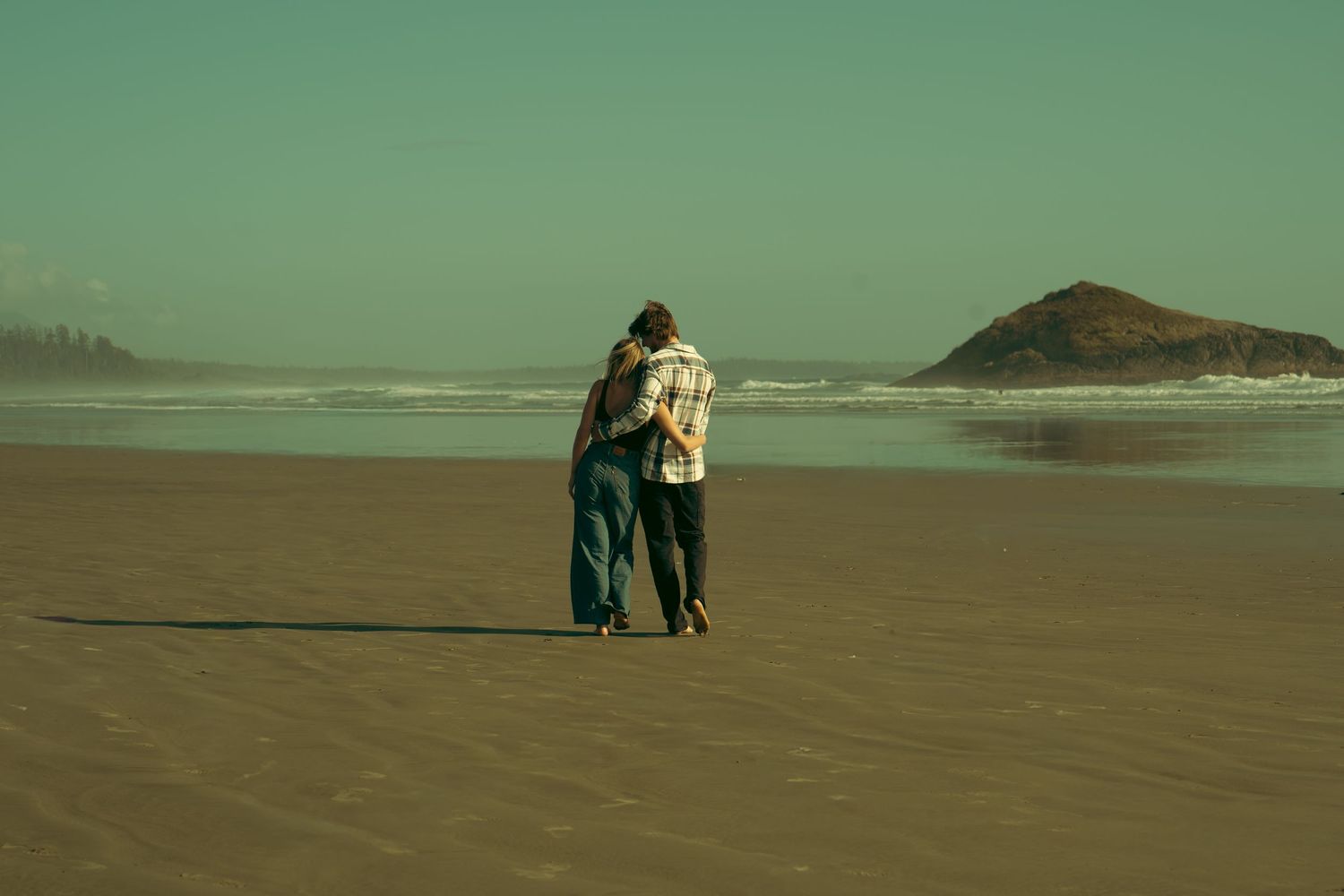 A couple embracing while walking along a misty beach shoreline.