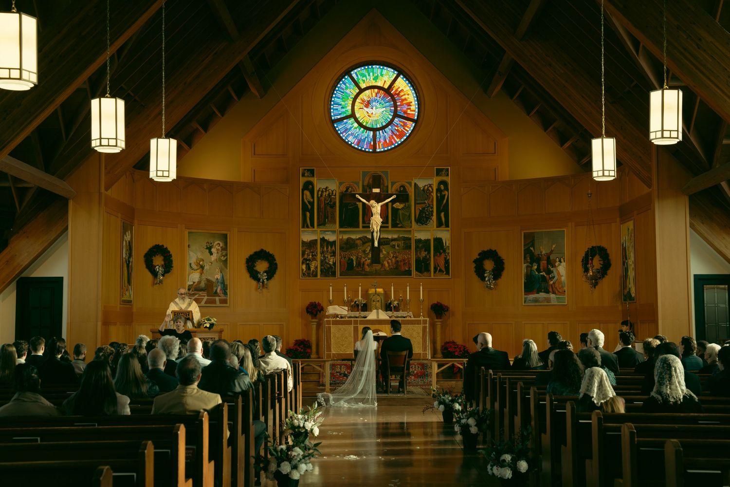 Interior of a church with stained glass windows and hanging lanterns during a wedding ceremony.