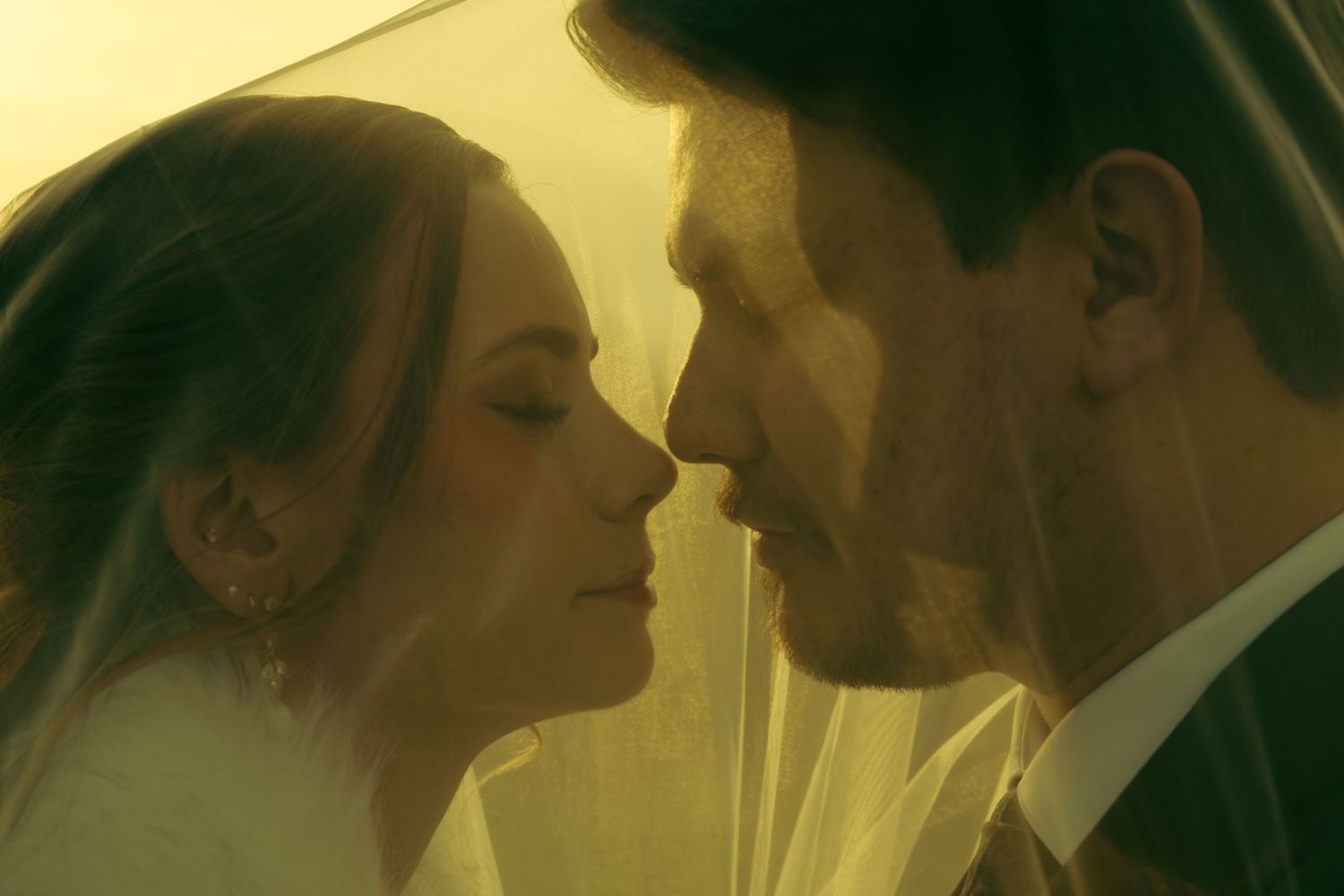 A romantic couple embraces in golden sunlight during an intimate moment outdoors.