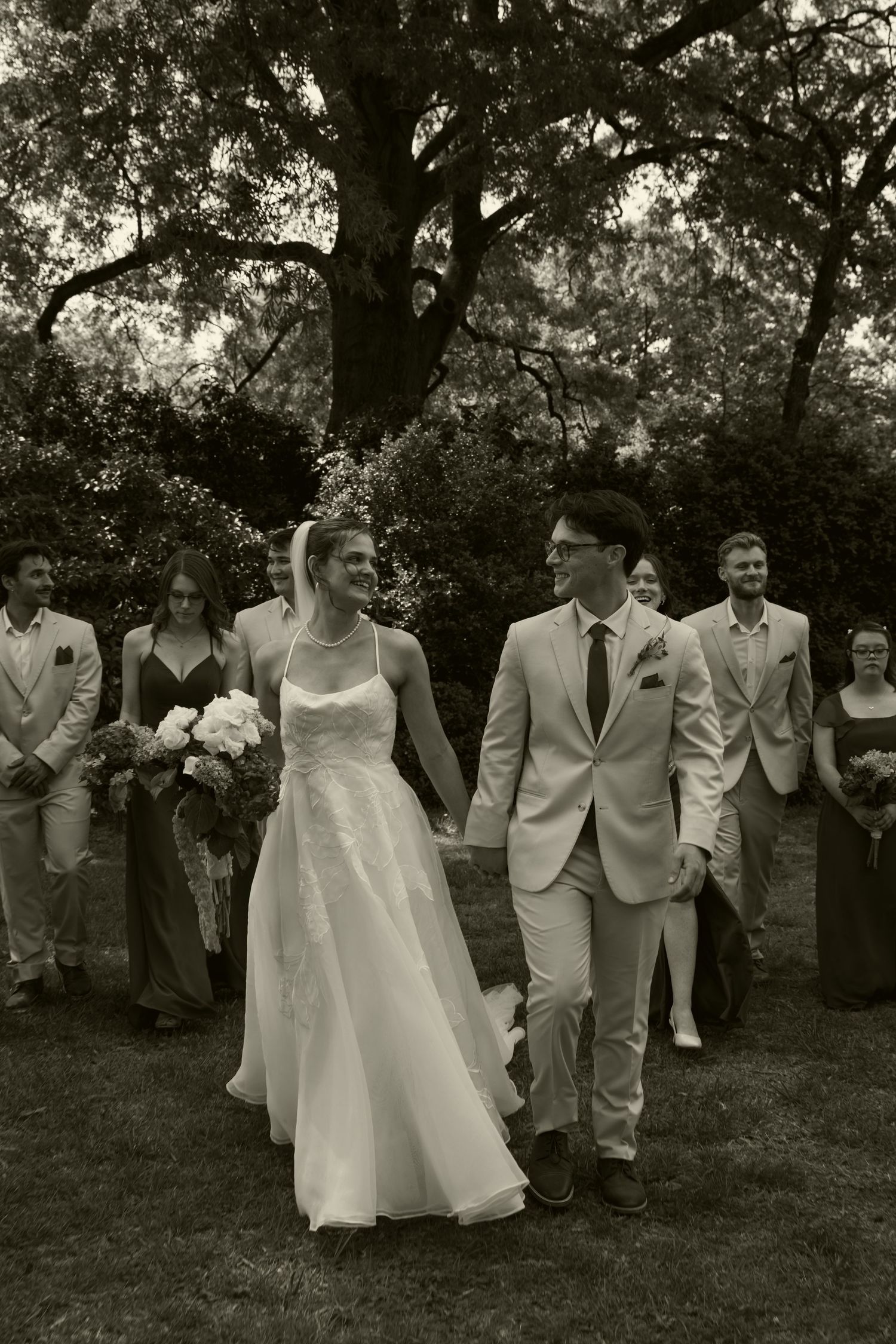 Black and white wedding party walking outdoors with bride and groom holding hands.