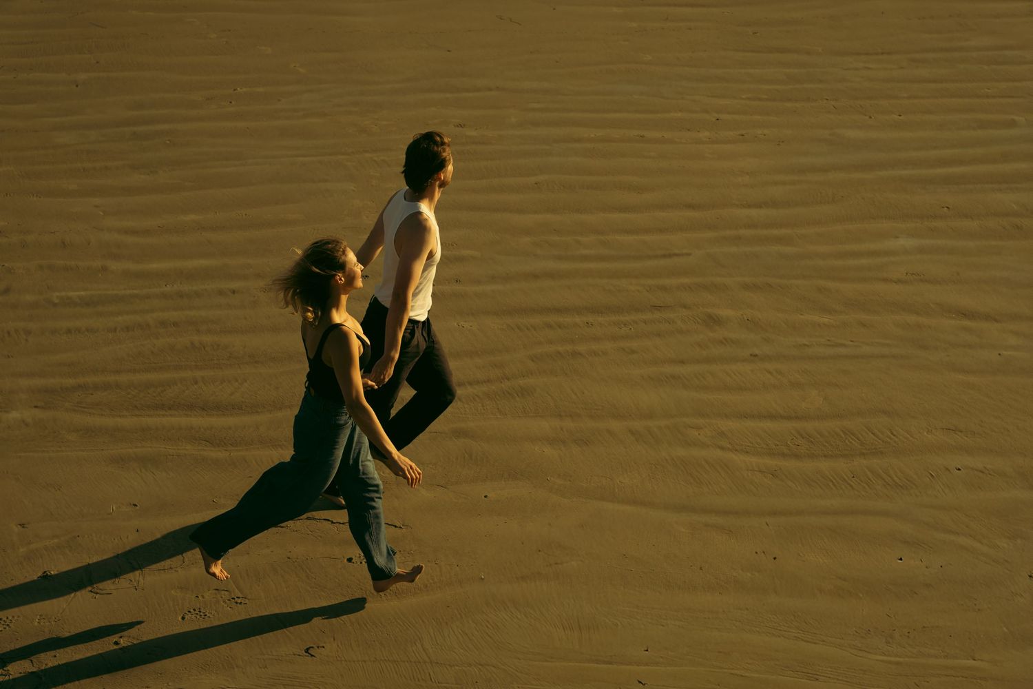 Two people walking together on golden sand during sunset.