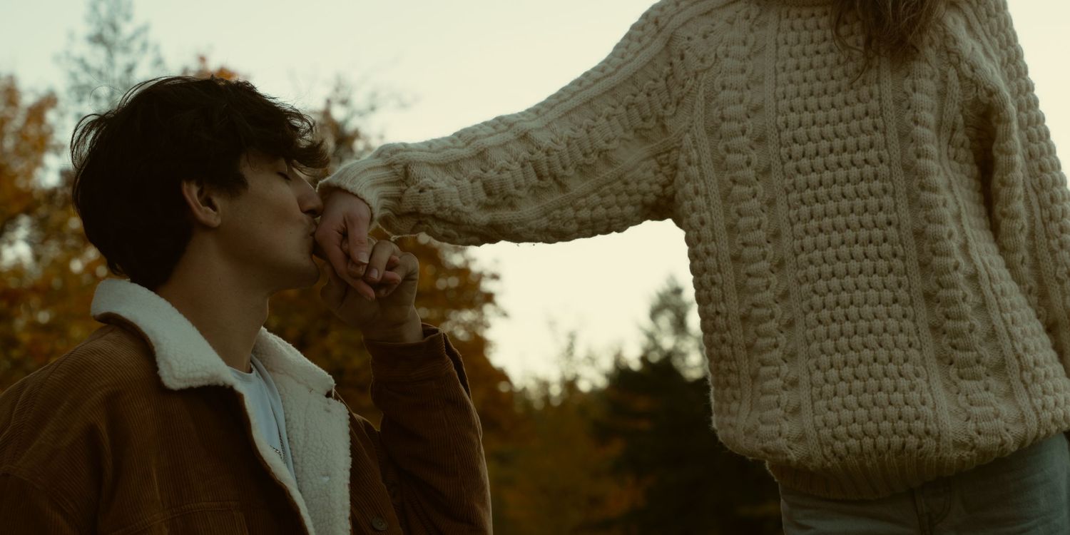Two people stand together in an autumn park with golden leaves and warm lighting.