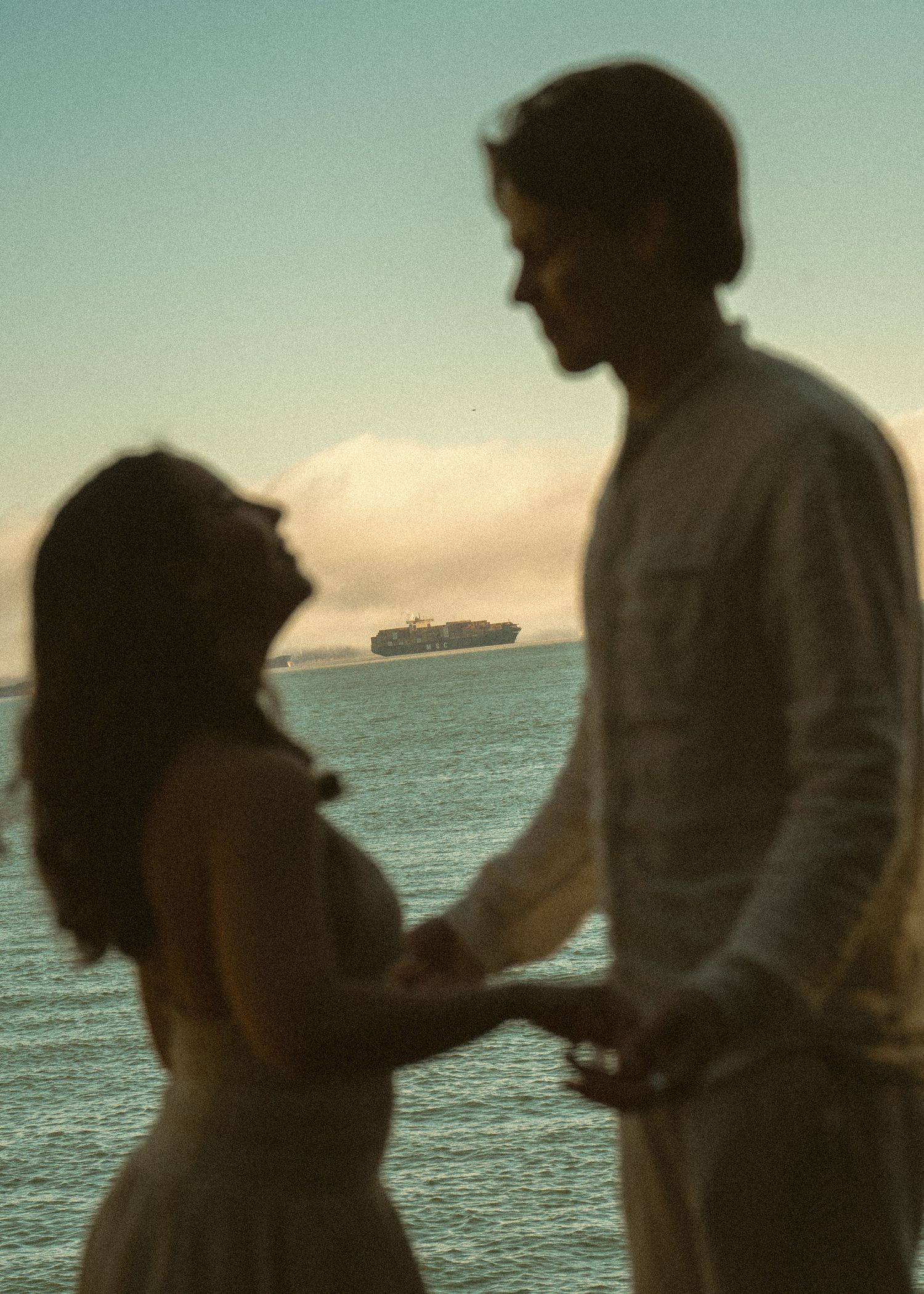 Silhouetted figures stand against an ocean horizon at sunset, examining something in their hands.