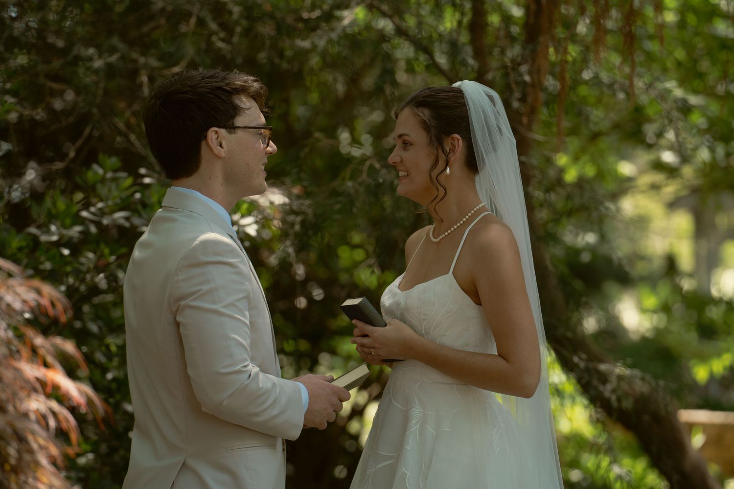 Bride and groom exchange vows outdoors in lush green garden wedding ceremony setting.