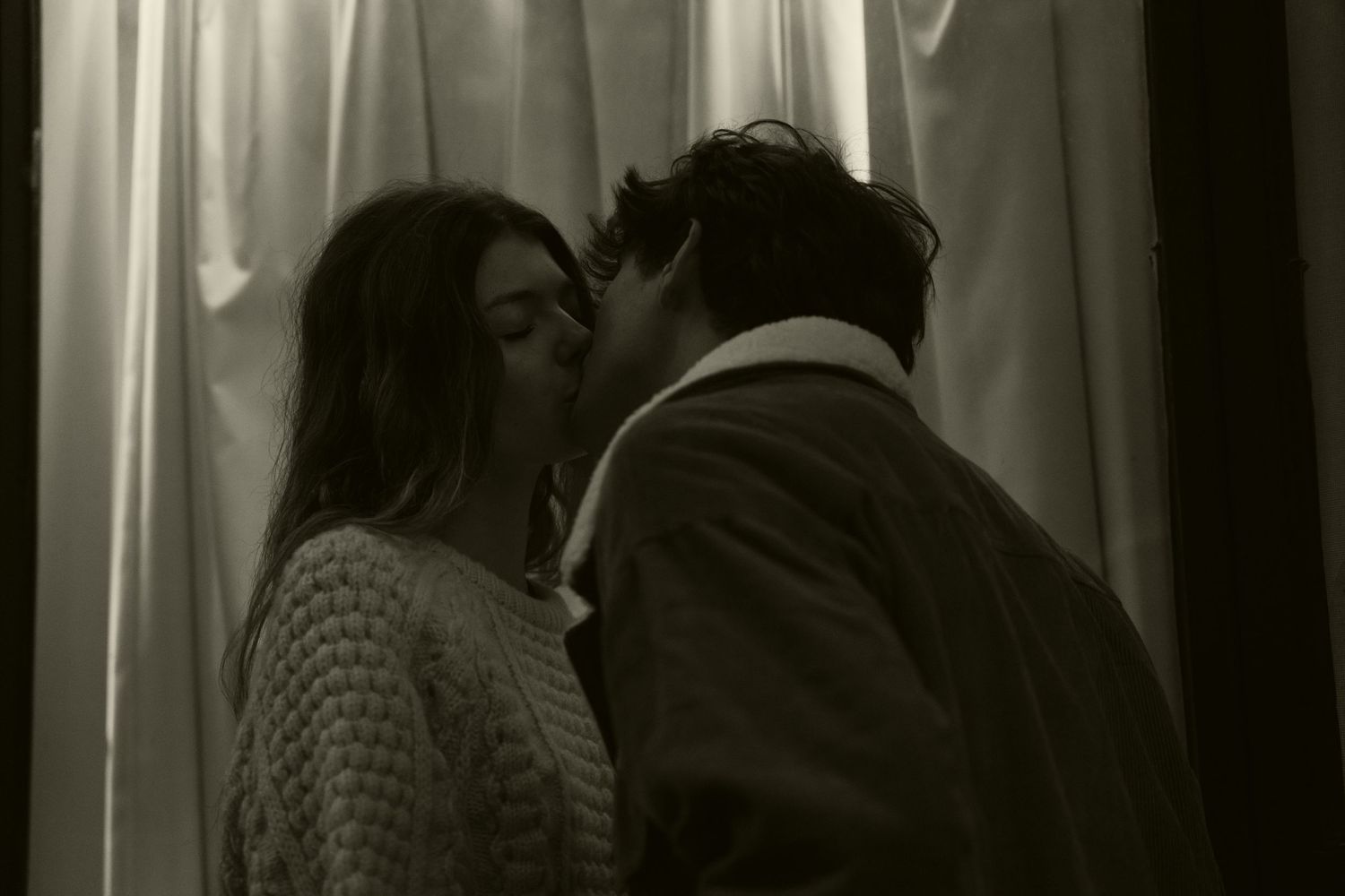 Intimate moment captured in black and white against illuminated curtains.