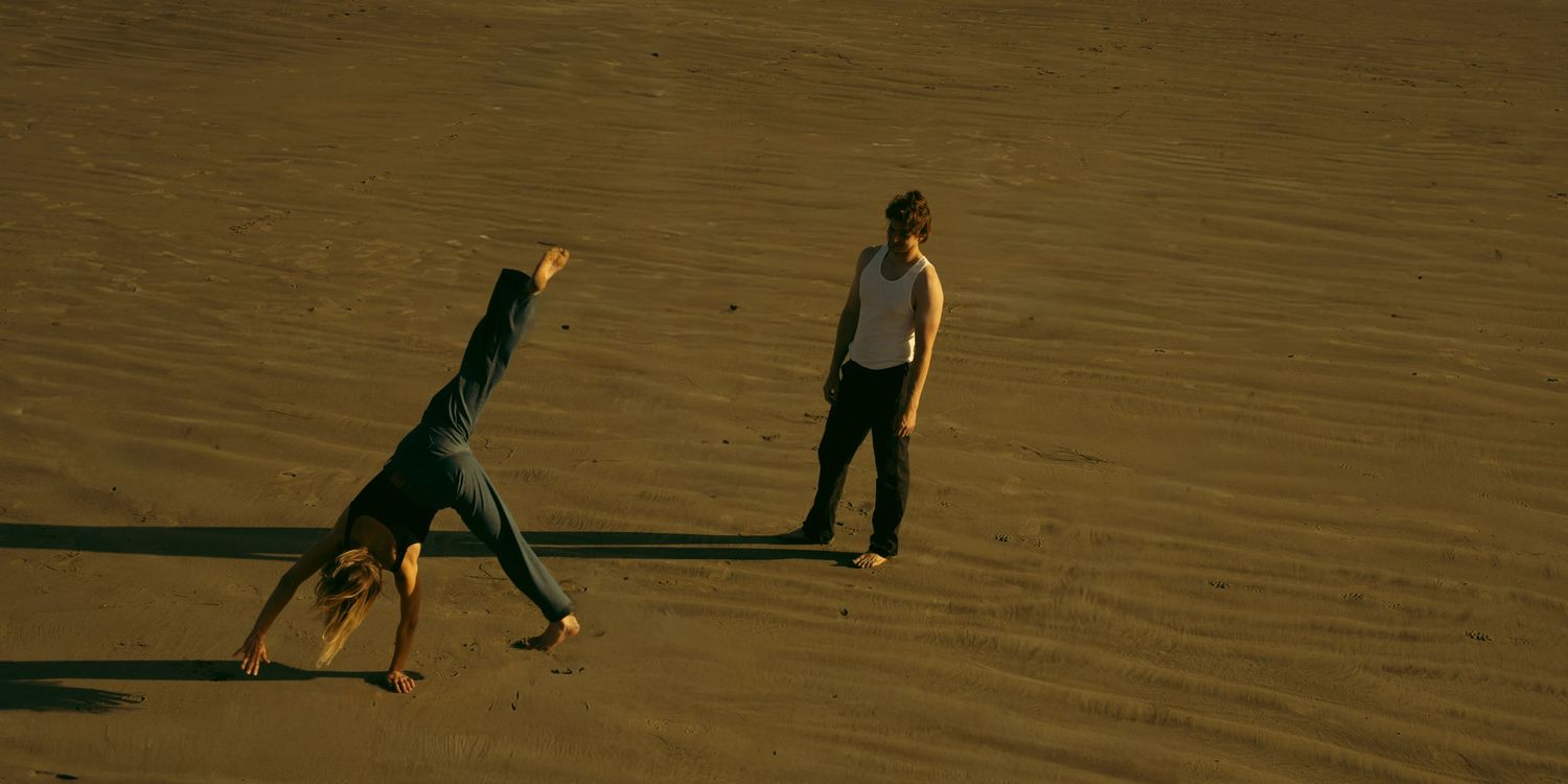 Two people on a beach at sunset, one doing a cartwheel.